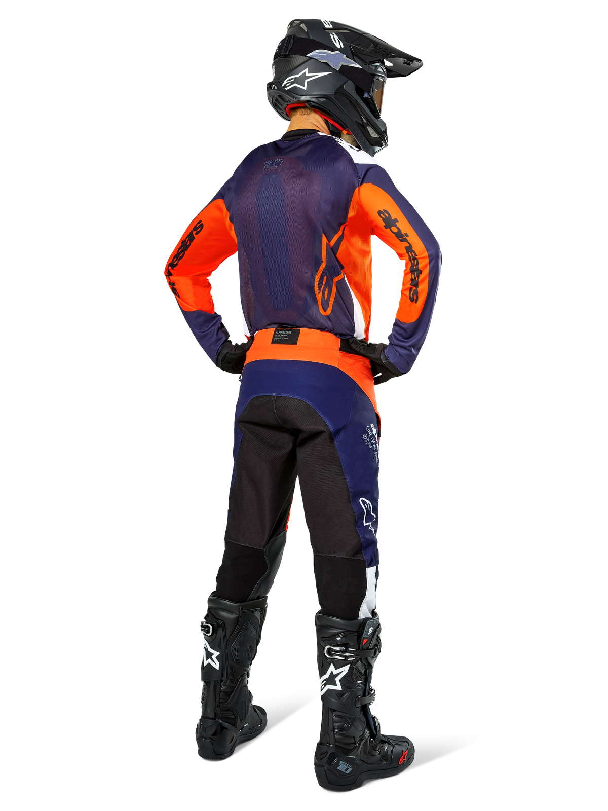 Alpinestars motocrossrijder van achteren gezien met volledige race-uitrusting, marineblauwe en oranje jersey, Pro-Dura broek in Navy Hot Orange White, zwarte helm en zwarte laarzen, professionele off-road race-outfit ensemble.