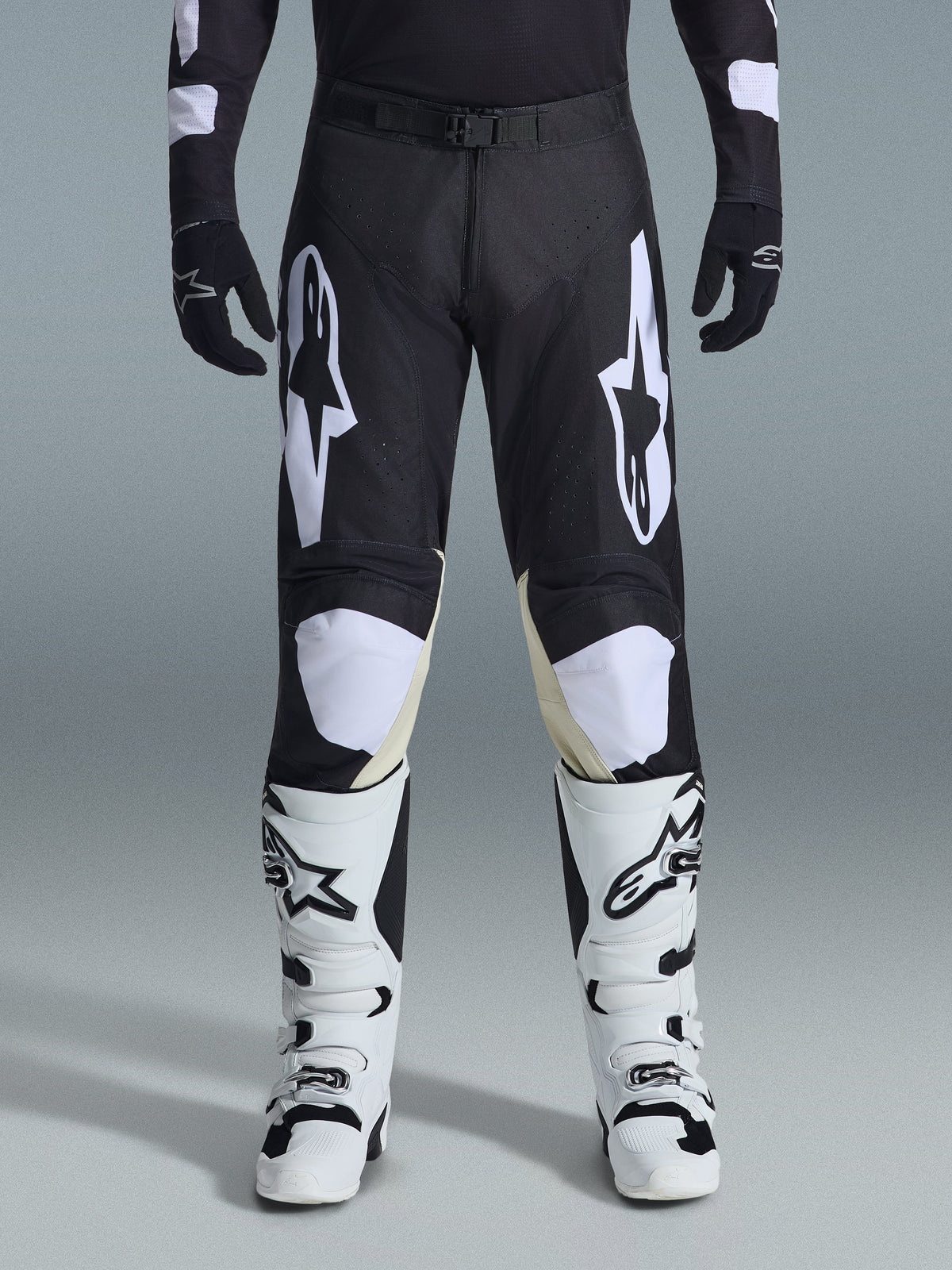 Alpinestars 2026 Racer Air Riway Pants, motorcrossbroek, zwart en wit, met opvallende witte Alpinestars-logo's op de dijen en kniepanelen, gecombineerd met wit-zwarte motorcrosslaarzen en zwarte handschoenen, atletisch race-fit ontwerp voor off-road rijden