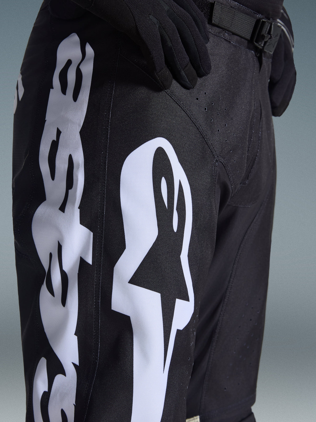 Alpinestars 2026 Racer Air Riway broek, motorcrossbroek, zwart en wit, detailweergave van grote witte Alpinestars-branding, lasergesneden perforaties voor luchtstroom en verstelbare gesp bij de taille, duurzaam materiaal voor off-road rijden