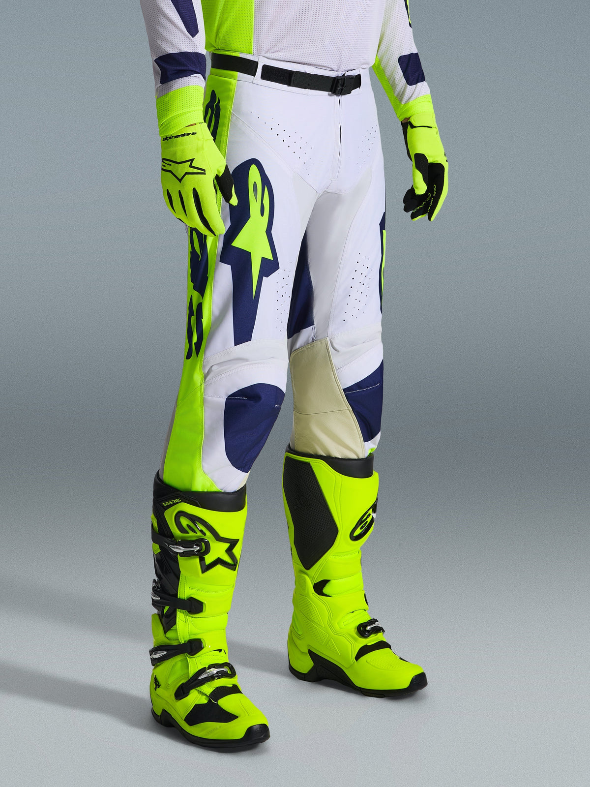 Alpinestars 2026 Racer Air Riway crossbroek, motorcross broek, lichtgrijs, fluogeel en blauw, gedragen met bijpassende fluogele handschoenen en laarzen, voorzien van een groot blauw logo op de dij en geperforeerde ventilatiepanelen, duurzame uitrusting voor motorcross.