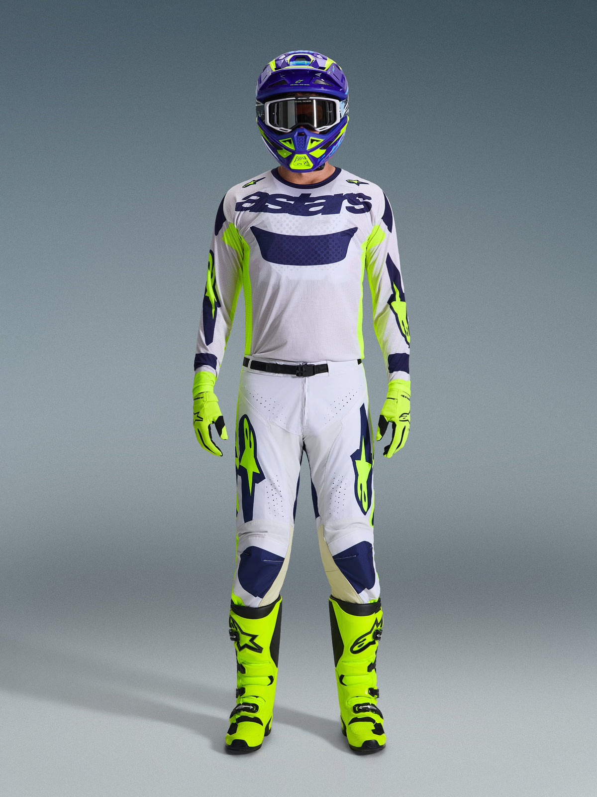 Alpinestars 2026 Racer Air Riway broek, motorcrossbroek, lichtgrijs met geel fluo en blauw, gedragen door een rijder in een volledige race-uitrusting met bijpassende witte jersey, fluoriserend gele laarzen en handschoenen en een blauwe helm, professionele off-road race-uitrusting