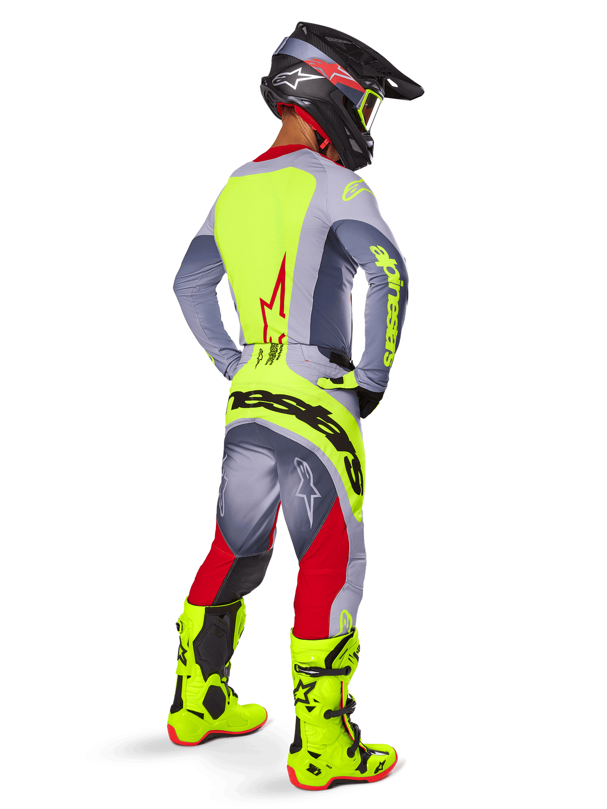 Motorcrosser in drie-kwart achteraanzicht, draagt Alpinestars 2025 Techstar Melt broek in felrood en grijs, met een opvallend neongeel logo op het zitvlak, bijpassende grijze en neongele jersey, felgekleurde neongele laarzen en een zwarte helm met neon crossbril, professionele off-road race-uitrusting.
