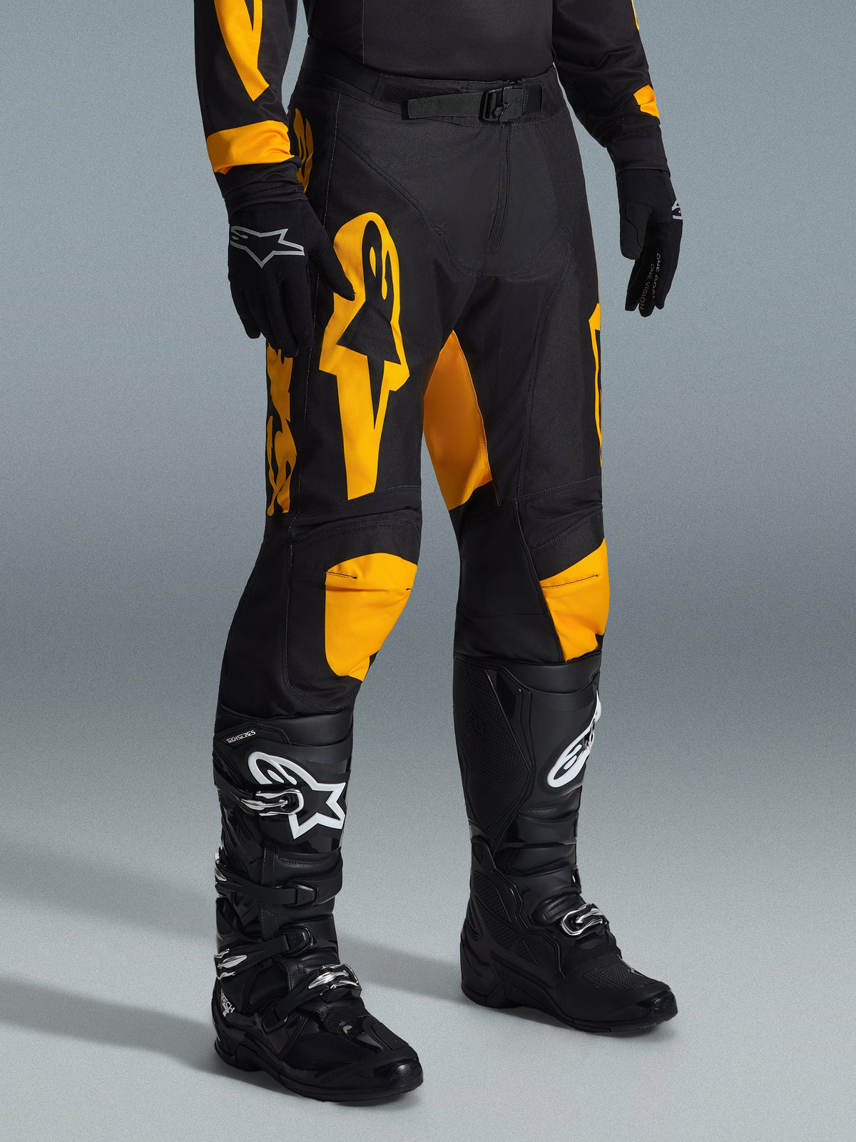 Alpinestars 2026 Racer Riway broek, motorcrossbroek, geel en zwart, gedragen met zwarte handschoenen en zwarte motorcrosslaarzen, met opvallende gele Alpinestars-branding en knie-accenten op een zwarte basis, ontworpen voor hoogwaardige off-road prestaties.