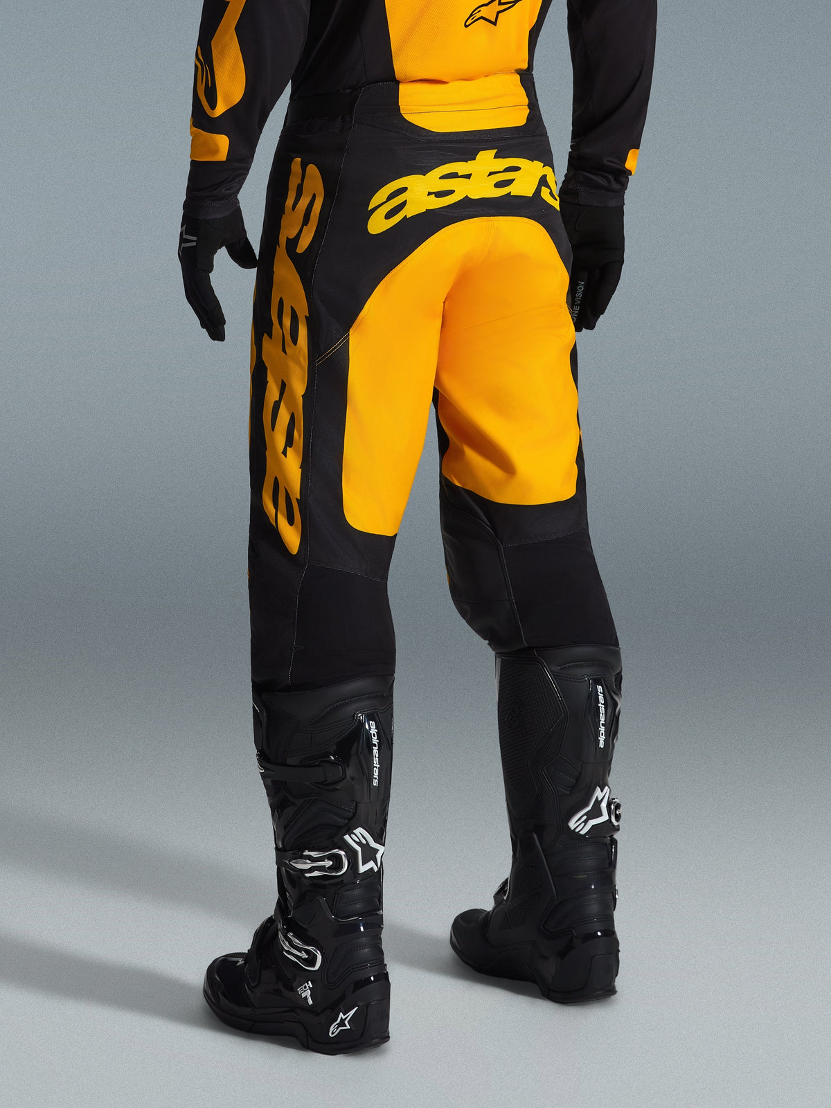 Alpinestars 2026 Racer Riway broek, motorcross broek, geel met zwart, achteraanzicht met opvallende gele astars-branding op het zitvlak en de broekspijp, gecombineerd met zwarte motorcrosslaarzen en handschoenen