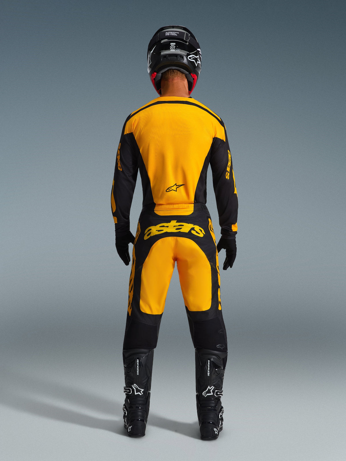 Motorcrosser van achteren gezien in Alpinestars 2026 Racer Riway broek en bijpassende jersey in geel en zwart, met opvallende gele branding op de achterkant, gecombineerd met een zwarte helm, zwarte handschoenen en zwarte motorcrosslaarzen, complete off-road race-uitrusting