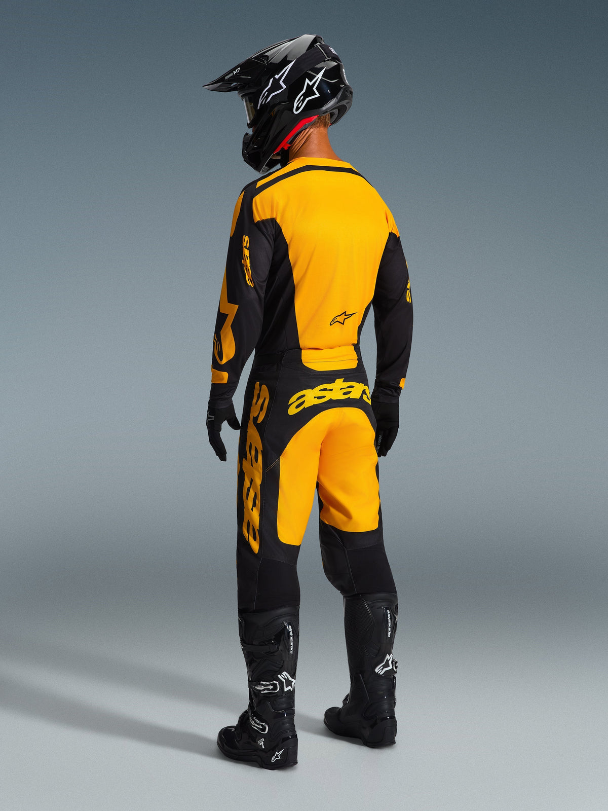 Achteraanzicht van een motorcrosser die de Alpinestars 2026 Racer Riway broek draagt in geel en zwart, met bijpassende jersey, zwarte helm en zwarte laarzen, gecoördineerde race-uitrusting voor off-road prestaties.