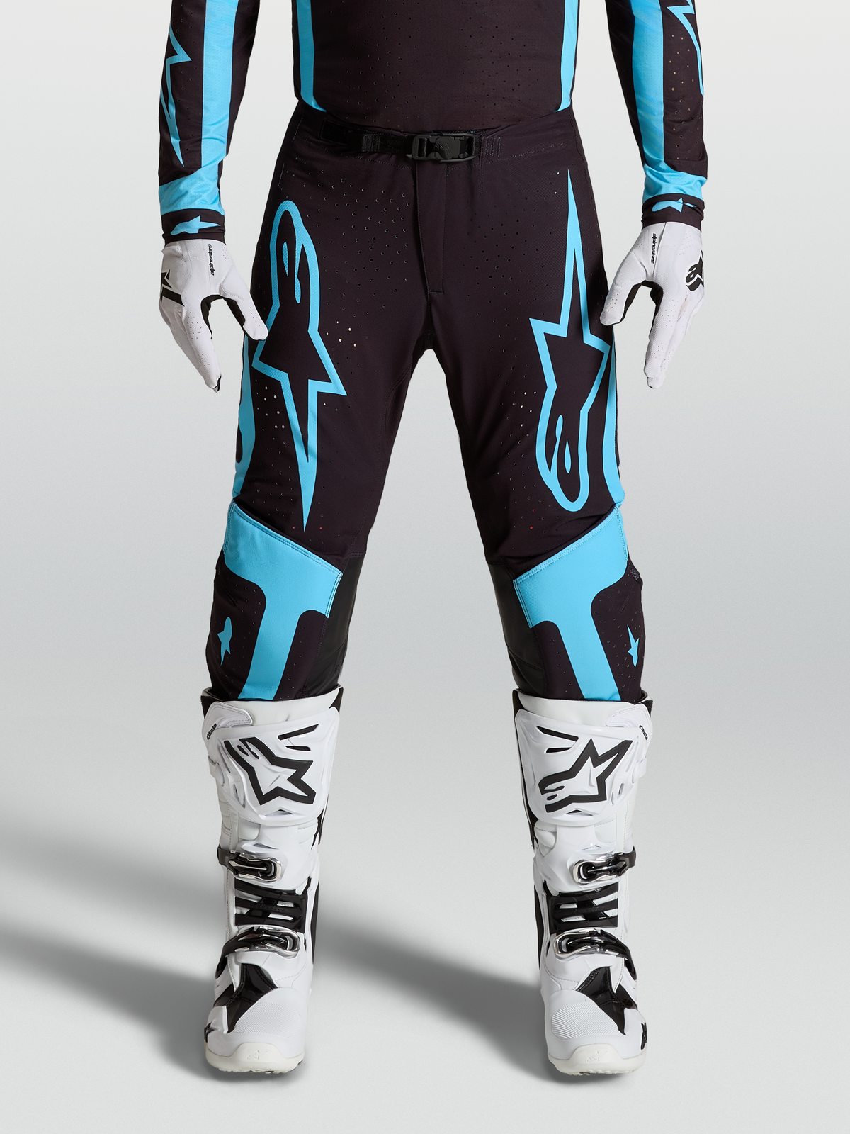 Alpinestars Supertech Vesta broek, professionele motocrossbroek, zwart en turquoise, gedragen door racer met witte laarzen en handschoenen.