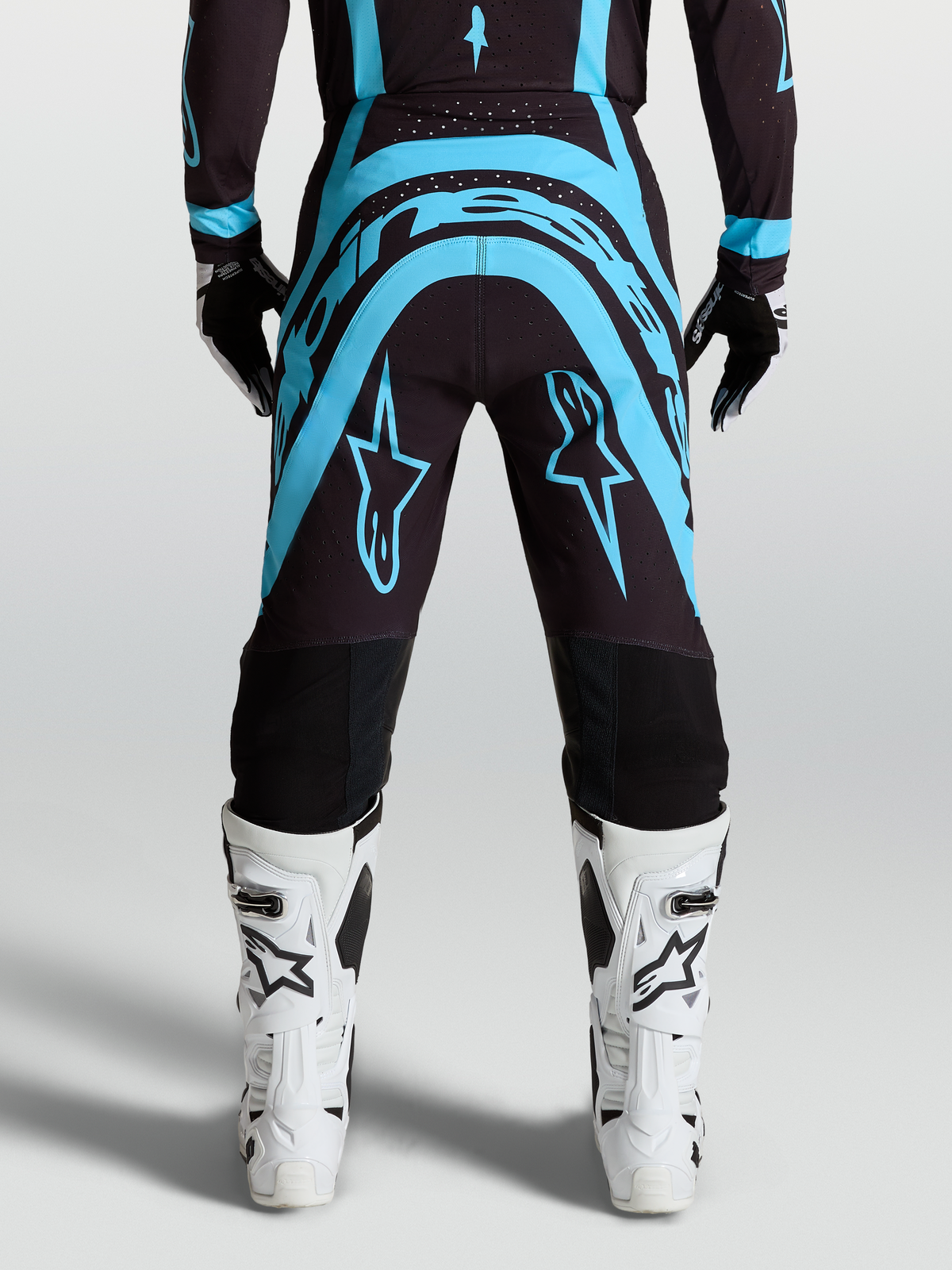 Alpinestars Supertech Vesta Broek, motocrossbroek in zwart en turquoise met witte motorlaarzen, race-fit.