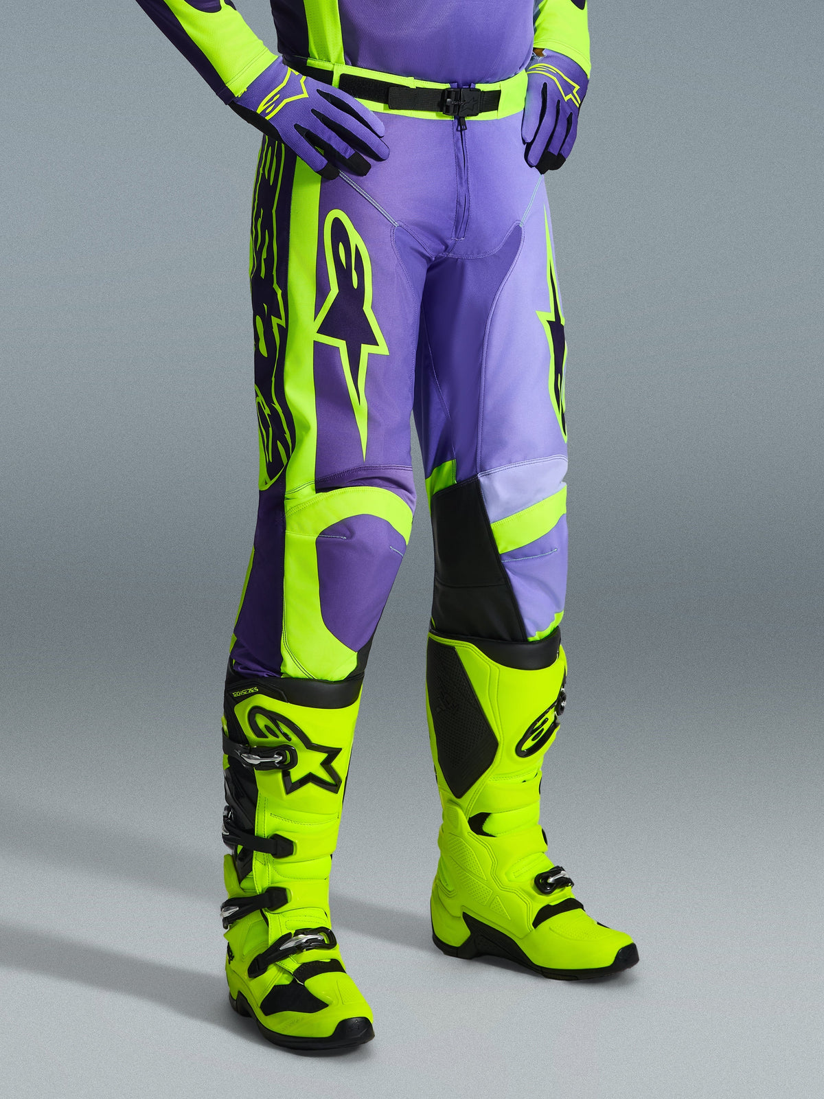Alpinestars 2026 Racer Portl Pants, motorcrossbroek in paars en fluogeel, gedragen door een rijder met bijpassende fluogele laarzen en paarse handschoenen, met opvallende Alpinestars-branding en ergonomisch ontwerp voor off-road prestaties