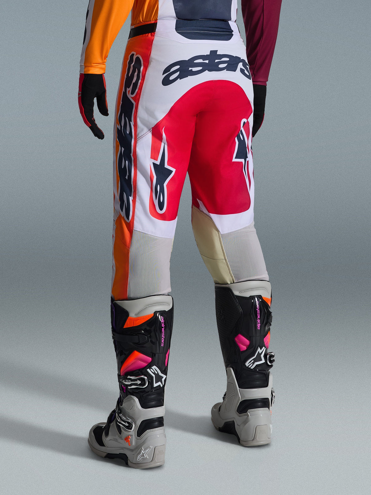 Alpinestars 2026 Racer Portl broek, motorcrossbroek, rood, lichtgrijs en donkergrijs, achteraanzicht met opvallende branding en logo-details, gecombineerd met bijpassende motorcrosslaarzen en handschoenen, performance-uitrusting voor off-road racen.