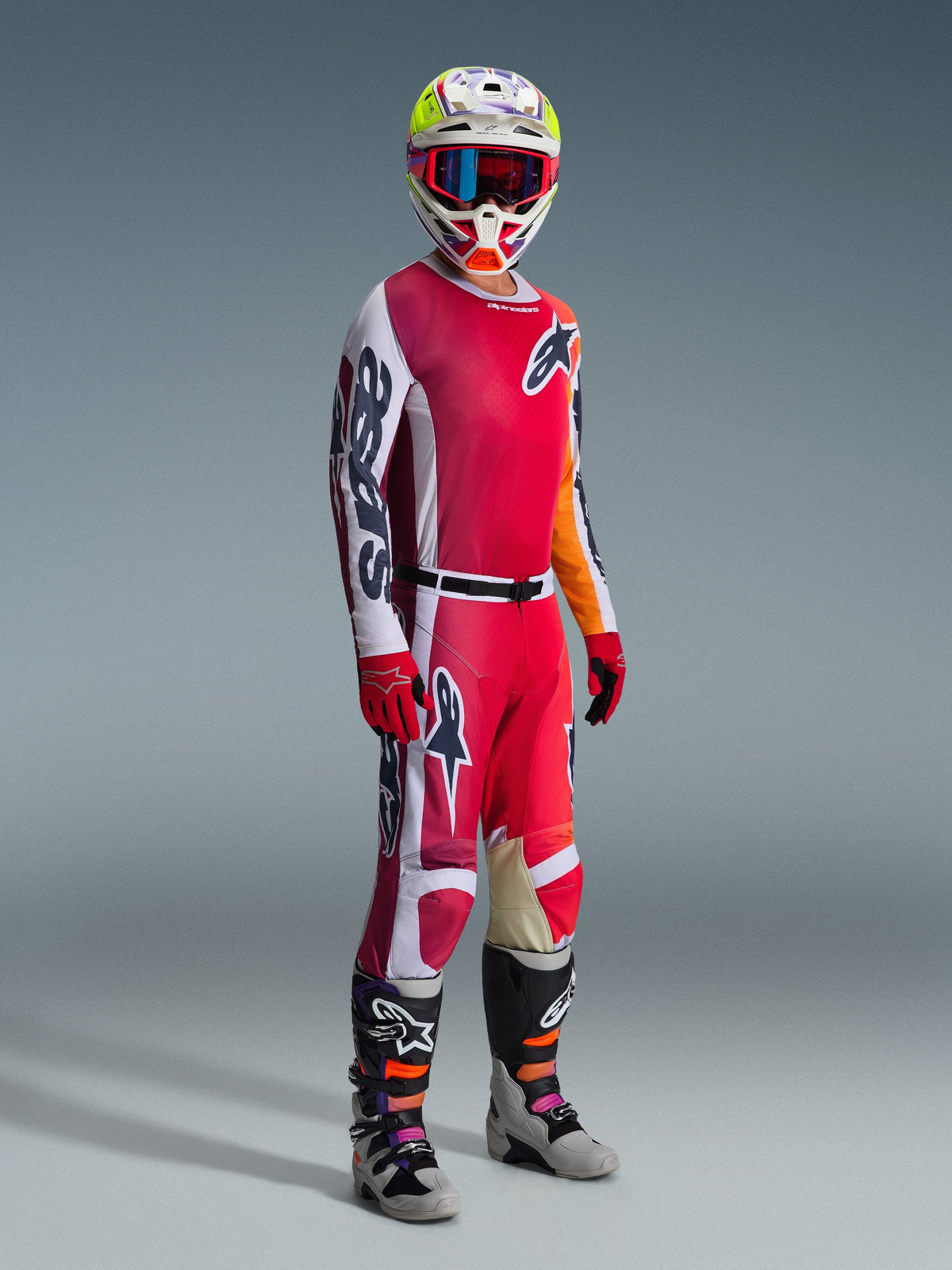 Alpinestars 2026 Racer Portl Pants, motorcrossbroek, rood, lichtgrijs en donkergrijs, gedragen als onderdeel van een volledige race-uitrusting met bijpassend shirt, rode handschoenen, kleurrijke helm met blauwe bril en grijze laarzen, duurzame constructie voor off-road motorcrossprestaties.