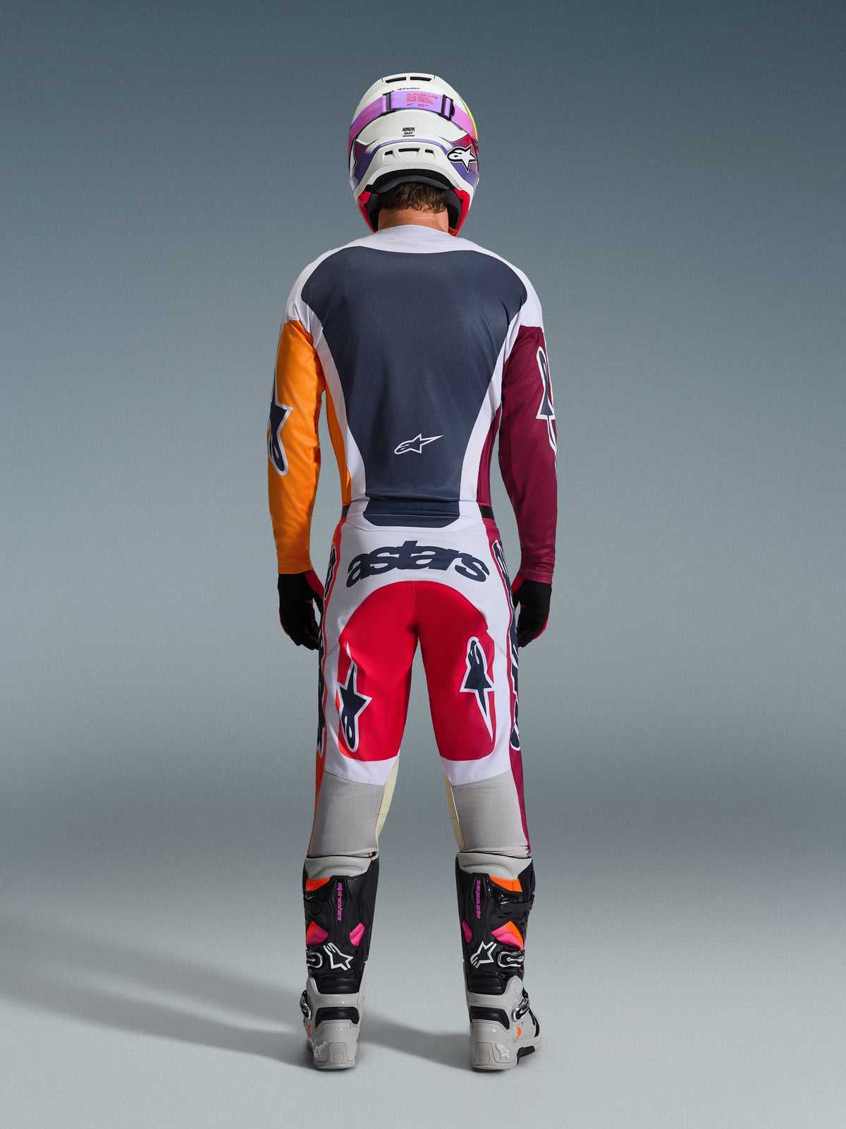Motocrosser van achteren gezien in de 2026 Racer Portl Broek in rood, lichtgrijs en donkergrijs, voorzien van 'astars' branding op het zitvlak, gecombineerd met een veelkleurig jersey, witte helm en technische racelaarzen.