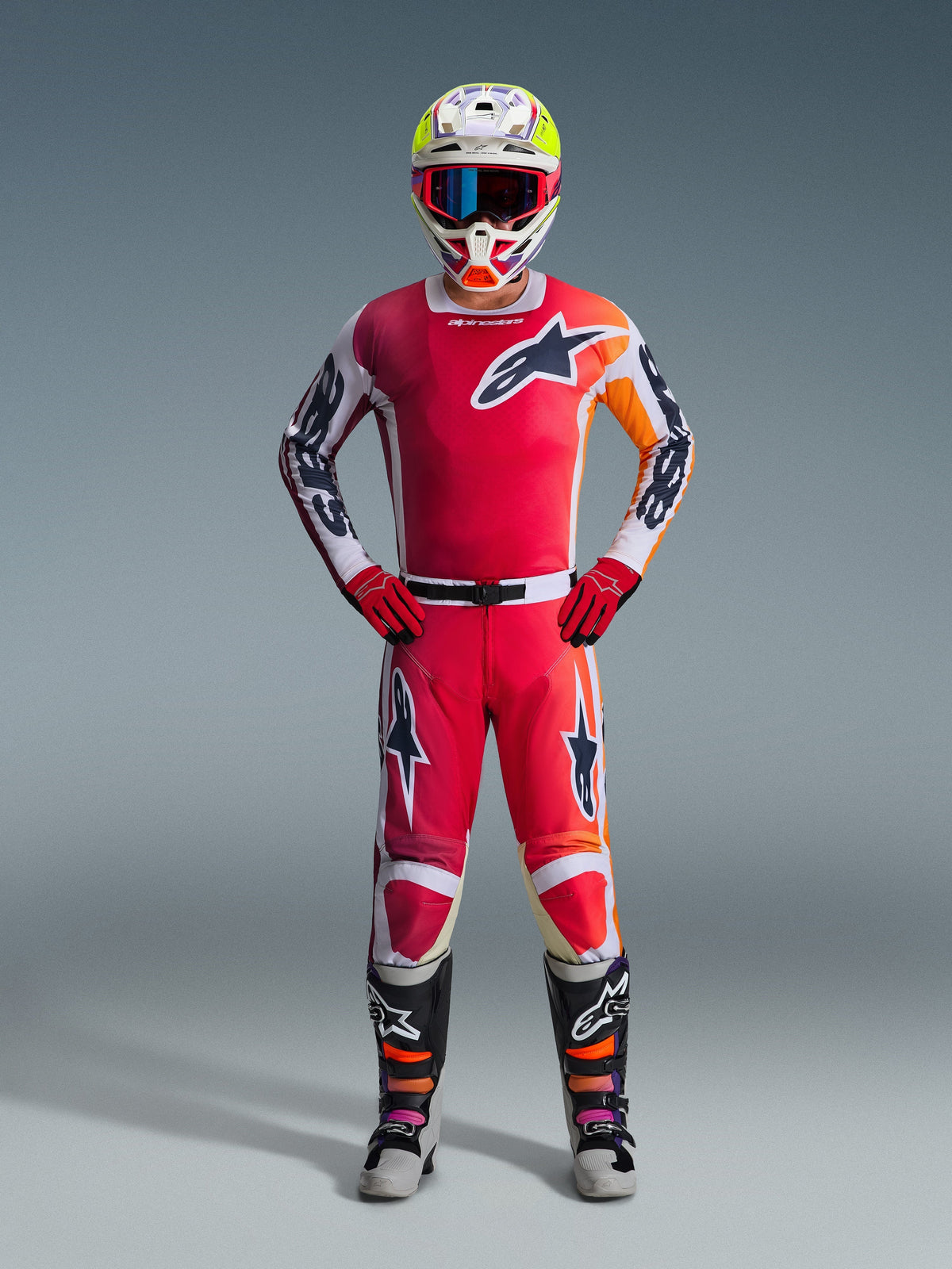 Motorcrosser in volledige race-uitrusting, rood jersey met witte en oranje accenten, 2026 Racer Portl-broek in rood en wit, witte helm met kleurrijke accenten en blauwe crossbril, rode handschoenen en zwarte en grijze laarzen, gecoördineerde outfit voor off-road prestaties