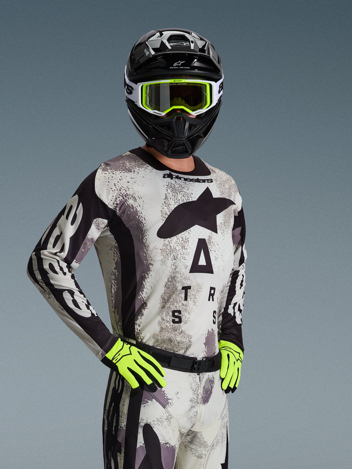 Motocrossrijder in de Alpinestars 2026 Racer Lahnd Jersey en kledingset, Sand Camo, lichtgrijs camouflagepatroon met zwarte logo's, zwarte helm met witte en neongele bril, fel neongele handschoenen, professionele off-road racekleding