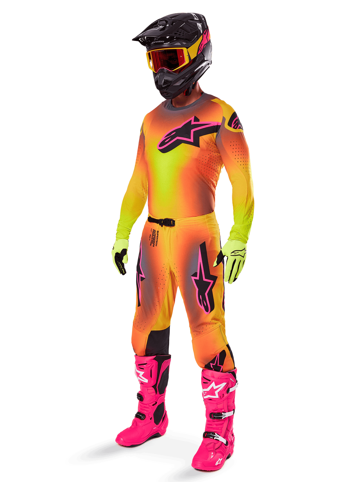 Alpinestars 2025 Supertech Lipan crossbroek, motorcross broek, geel en roze, gedragen als onderdeel van een volledige uitrusting met bijpassende jersey met kleurverloop, felroze laarzen, gele handschoenen en zwarte helm, voorzien van opvallende zwarte logo's en sportieve pasvorm voor off-road racen