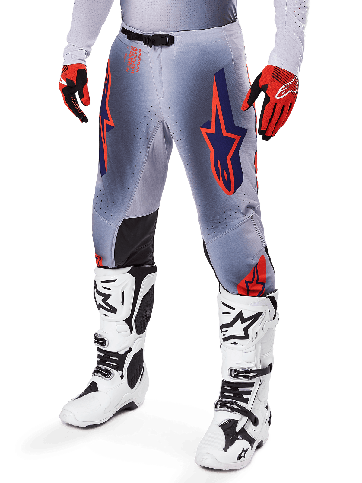 Alpinestars 2025 Supertech Lipan broek, motorcrossbroek, grijs en fluoriserend oranje, met donkerblauwe sterren en zwarte binnenkniepanelen, gedragen met roodoranje handschoenen en witte laarzen, professionele off-road race-uitrusting