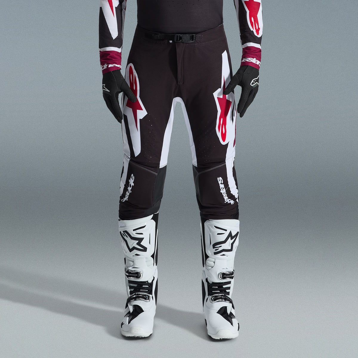 Alpinestars 2026 Supertech AFD Vista Gear Set, motocrossrijder in zwarte broek met grote witte en rode logo's, bijpassende performance jersey met bordeauxrode manchetten, zwarte handschoenen en witte professionele racelaarzen, hoogwaardige off-road race-outfit