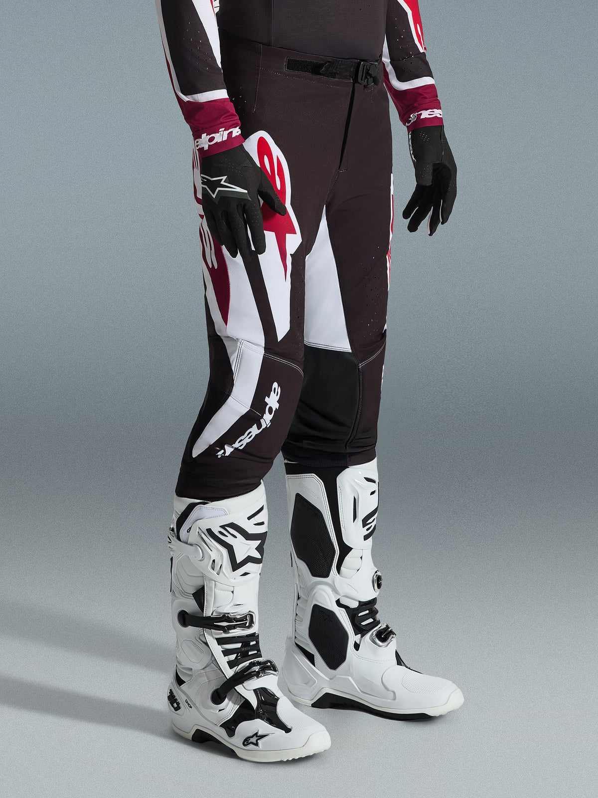Alpinestars 2026 Supertech AFD Vista Pants, motorcrossbroek, zwart, rood en wit, gedragen met witte en zwarte motorcrosslaarzen en zwarte handschoenen, met grote witte en rode grafische patronen, atletisch race-pasvorm ontwerp
