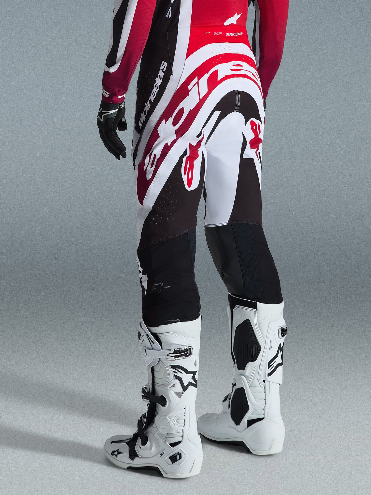 Alpinestars 2026 Supertech AFD Vista Broek, motocrossbroek, zwart, rood en wit, achteraanzicht met groot Alpinestars-logo op het zitvlak, gecombineerd met witte Tech 10 laarzen en zwarte handschoenen, sportief ontwerp voor elite off-road prestaties
