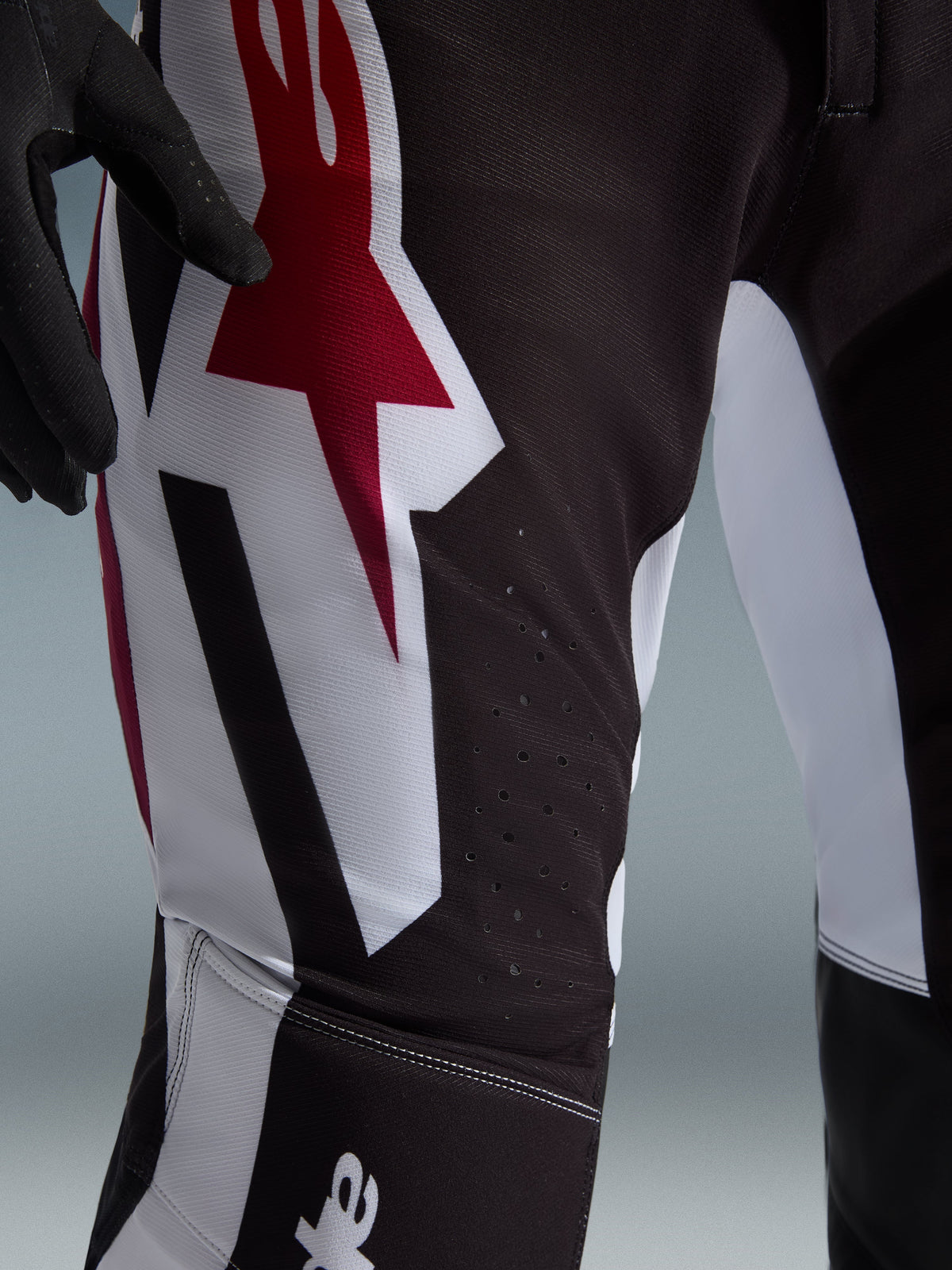 Alpinestars 2026 Supertech AFD Vista broek, motorcross broek, zwart, rood en wit, close-up van de dij met een groot rood en wit Astars-logo en laser-gesneden perforaties voor ventilatie.
