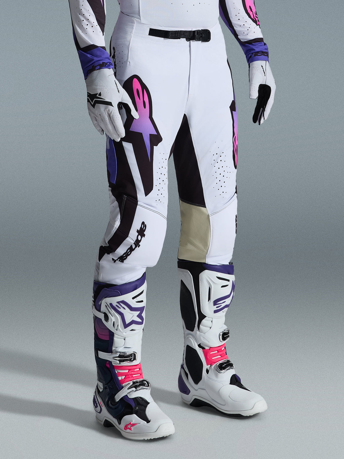 Alpinestars Supertech AFD Vista Broek 2026, motorcrossbroek, wit, paars en zwart, voorzien van een Astar-logo met roze en paars kleurverloop, gedragen met bijpassende witte en paarse motorcrosslaarzen en handschoenen, atletische racepasvorm met lichtbruine lederen binnenkniepanelen en geperforeerde details.