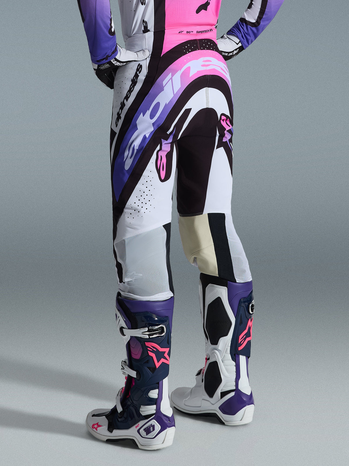 Alpinestars 2026 Supertech AFD Vista Broek, motorcrossbroek, wit, paars en zwart met roze accenten, achteraanzicht gedragen met bijpassend shirt en Tech 10 laarzen, voorzien van opvallende logo-graphics en hoogwaardige materialen voor elite off-road racing.