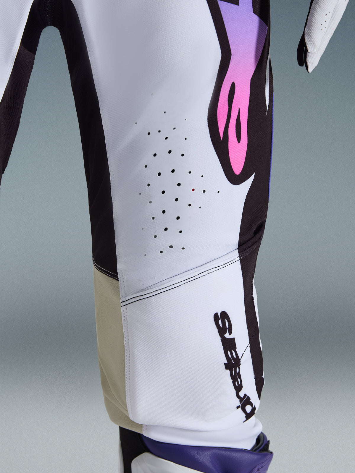 Alpinestars 2026 Supertech AFD Vista broek, motorcrossbroek, wit, paars en zwart, close-up met lasergesneden ventilatiegaten, verticaal Alpinestars-logo en beige binnenkniepanelen, hoogwaardige racekleding