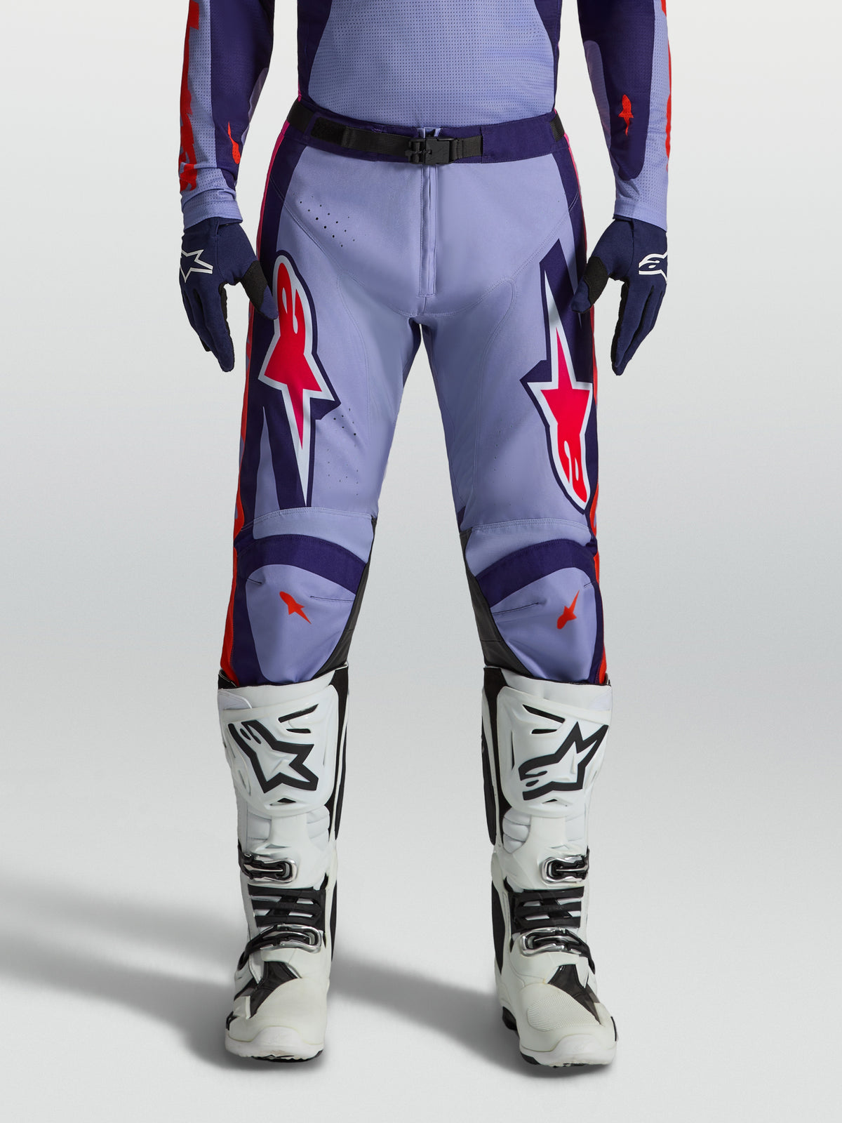 Alpinestars Racer Air Hunt broek, motorcrossbroek voor heren, lichtviolet en paars met roze fluo accenten, gedragen met witte motorlaarzen, geventileerd ontwerp.