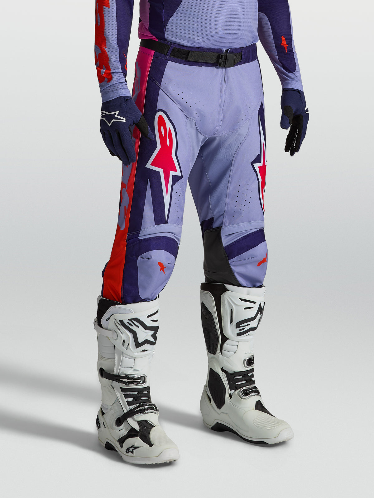 Alpinestars Racer Air Hunt Broek, geventileerde paarse en roze motorcrossbroek gedragen door een model met witte motorlaarzen, technische off-road race-uitrusting.