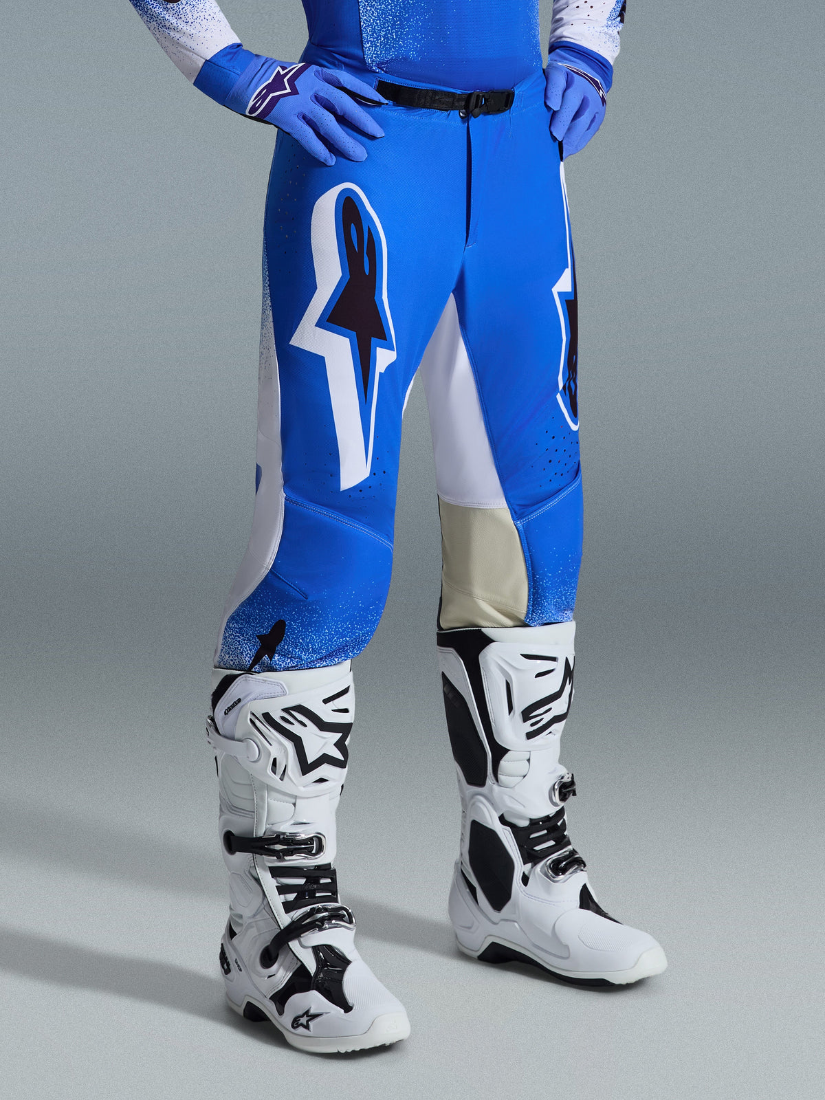 Alpinestars 2026 Supertech Scenz broek, motorcrossbroek, Ucla blauw en wit, gedragen met witte en zwarte laarzen en blauwe handschoenen, voorzien van grote grafische logo's op de dijbenen en witte panelen, atletische pasvorm ontworpen voor competitief motorcrossen