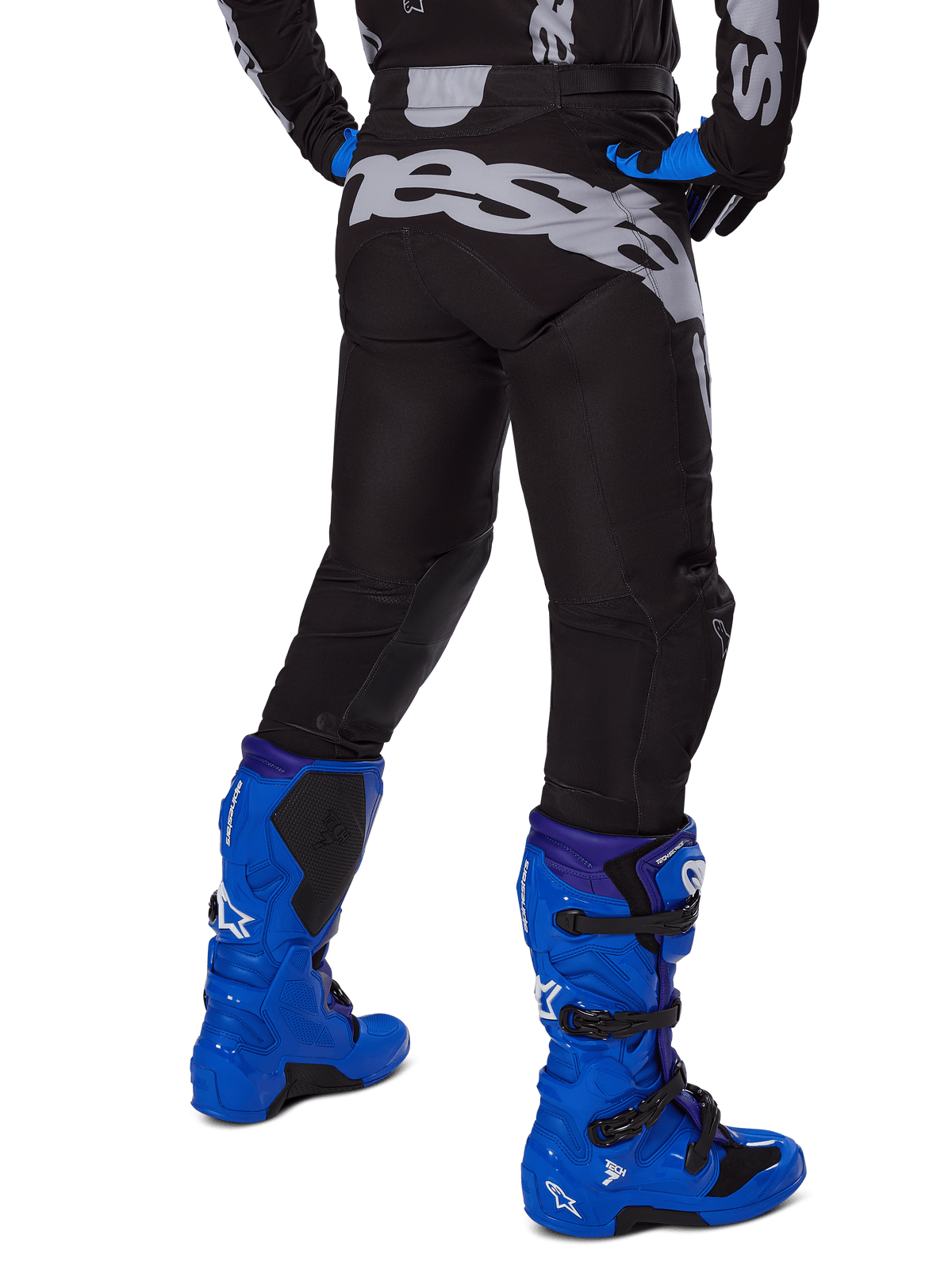 Alpinestars 2025 Racer Graphite broek, motorcrossbroek, zwart en grijs, achteraanzicht met grote grijze branding op het zitvlak, gedragen met felblauwe motorcrosslaarzen en een zwart-blauw jersey, duurzame off-road race-uitrusting