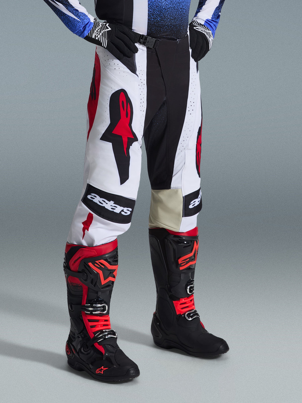 Alpinestars 2026 Techstar Knif Gear Set, motorcrossbroek en laarzen, wit, zwart en rood, met opvallende logo's en een constructie van verschillende materialen, gedragen met zwarte handschoenen, professionele race-uitrusting voor off-road prestaties.