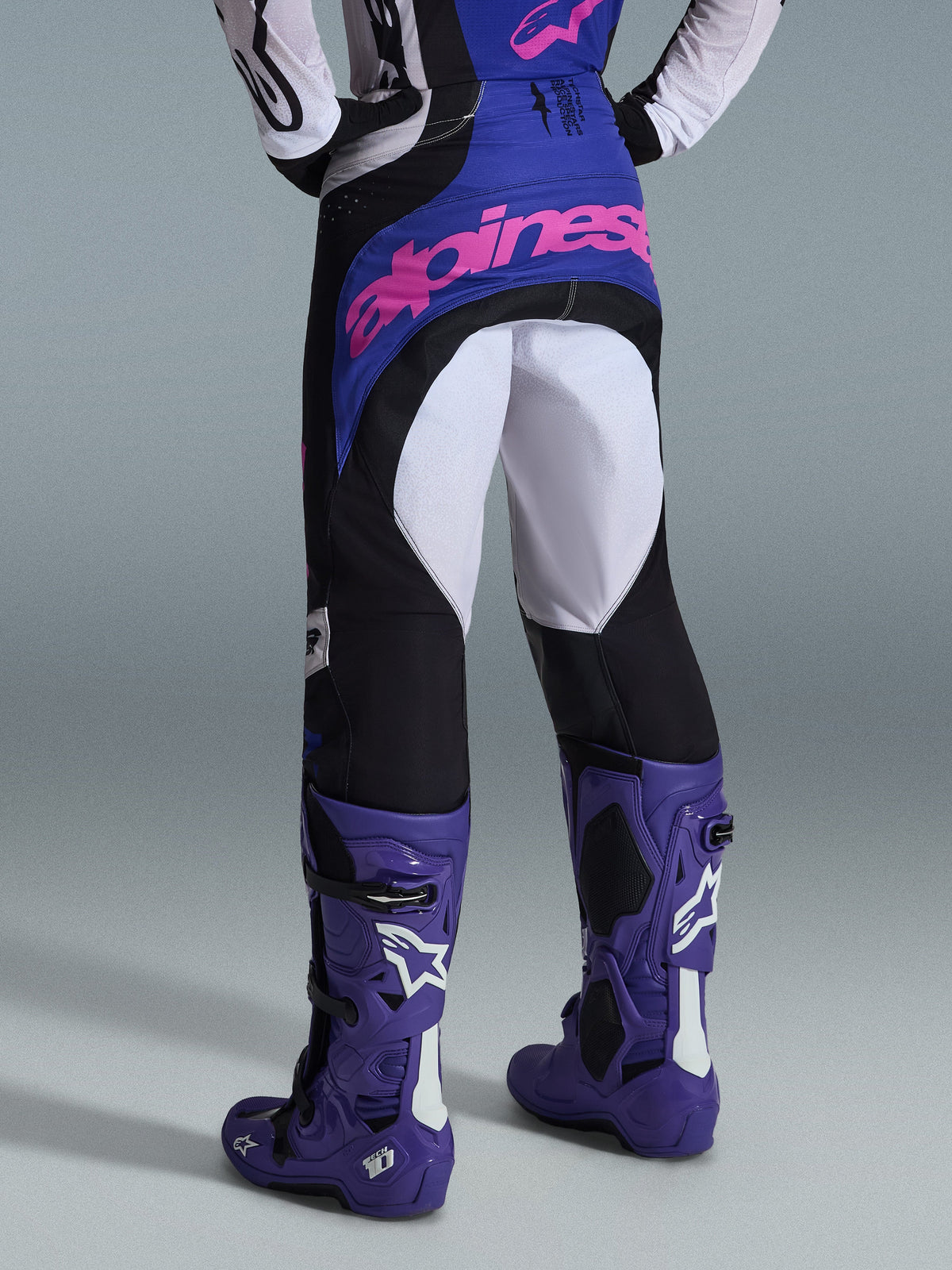 Alpinestars 2026 Techstar Knif crossbroek, motorcross broek, zwart, lichtgrijs en paars, achteraanzicht met roze branding op het zitvlak, gedragen met bijpassende jersey en paarse motorcrosslaarzen, professionele off-road race-outfit