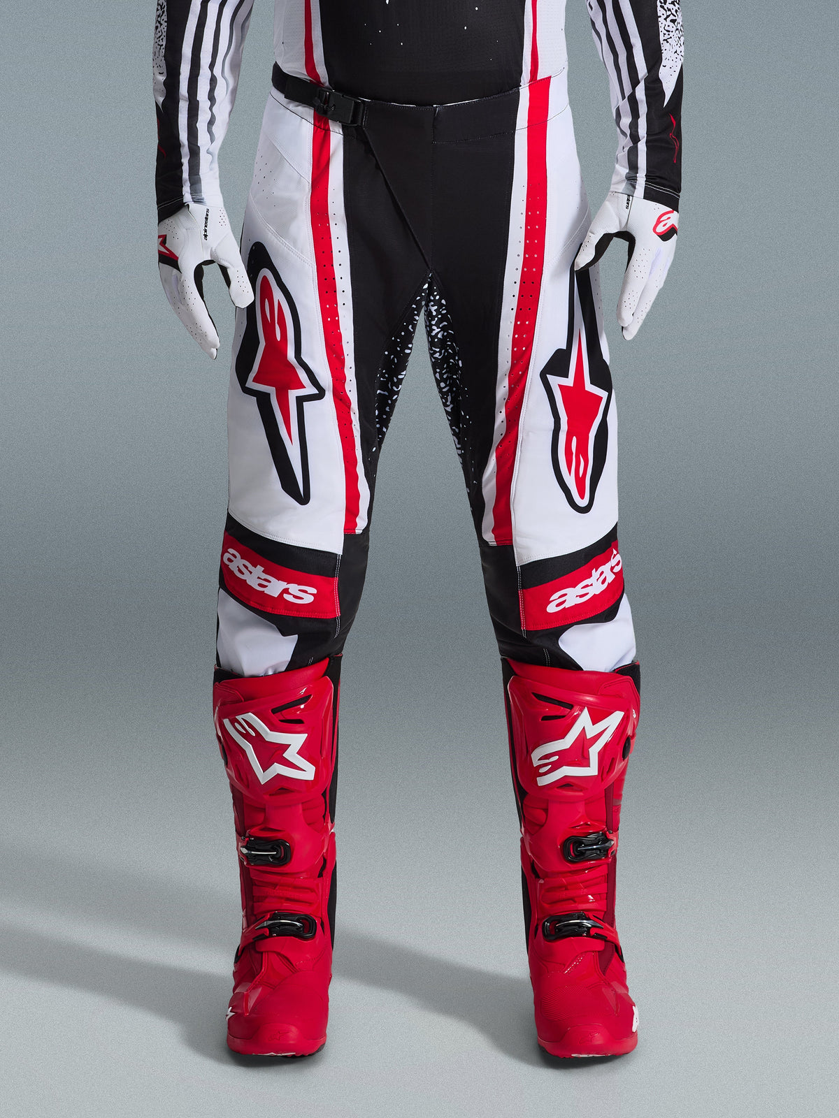 Alpinestars 2026 Techstar Nomur crossbroek, motorcross broek, zwart wit en rood, gedragen met bijpassende rode laarzen en witte handschoenen, met opvallende rode logo's op de dijen en 'astars' branding op de knieën, meerpanelen race-ontwerp voor off-road prestaties