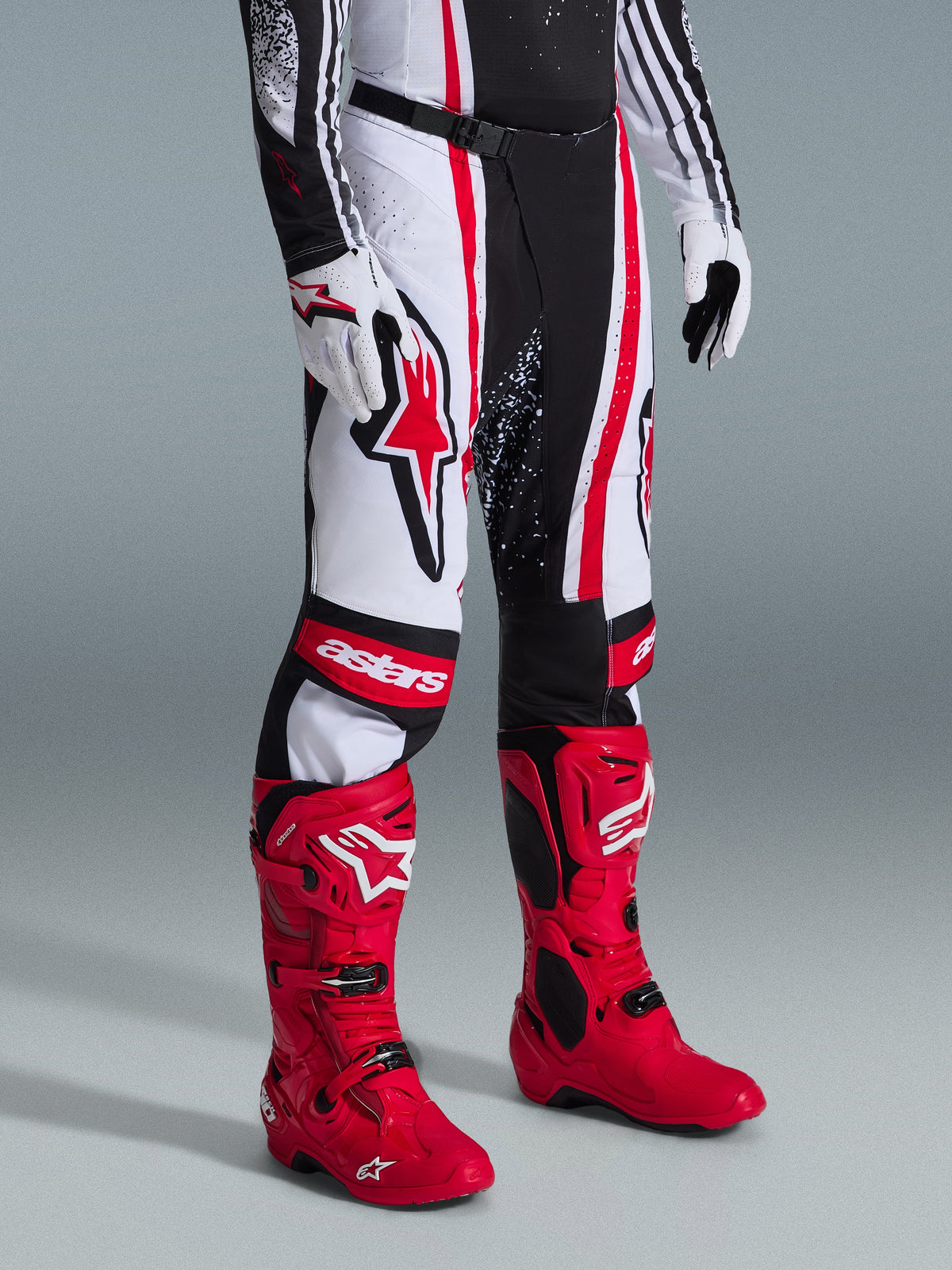 Alpinestars 2026 Techstar Nomur crossbroek, motorcross broek, zwart wit rood, gedragen met felrode racelaarzen en witte handschoenen, voorzien van opvallende verticale strepen, een groot rood sterlogo op de dij en versterkte kniepanelen voor off-road prestaties