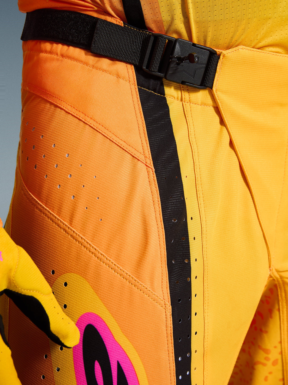 Alpinestars 2026 Techstar Nomur broek, motorcrossbroek, oranje geel roze, close-up van de taille met de SX2 magnetische gespsluiting, zwarte verstelband en lasergesneden ventilatieperforaties op duurzaam ripstop-materiaal