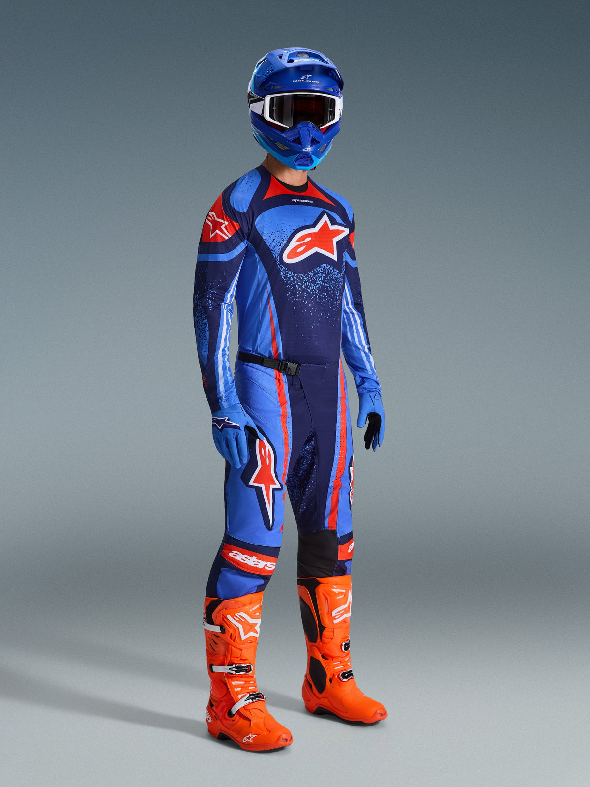Alpinestars 2026 Techstar Nomur Pants, Motocross Pants, Dark Navy Orange and UCLA Blue, worn by a rider in complete racing gear including a matching jersey, blue helmet, and bright orange boots, performance-engineered for off-road racing