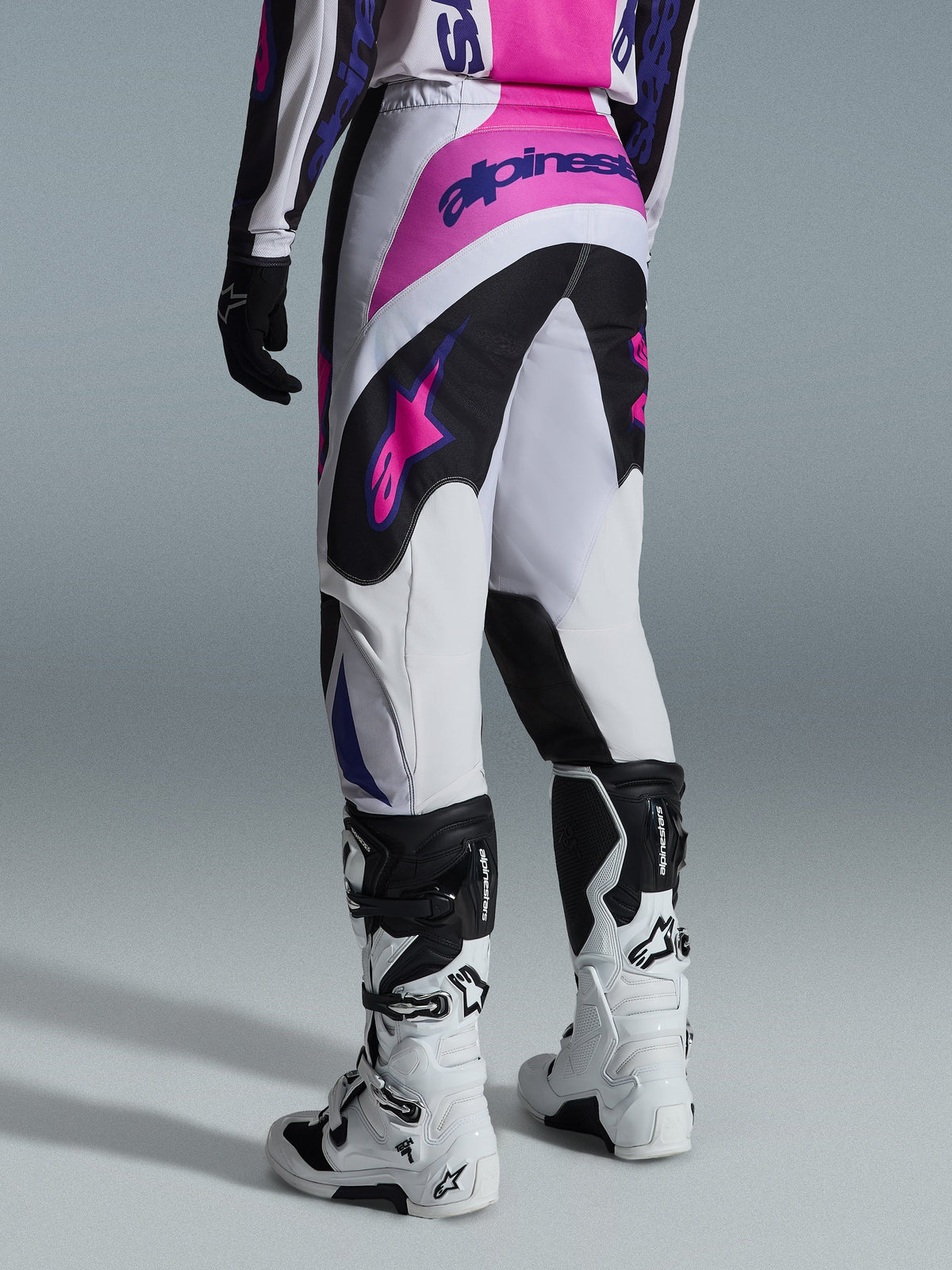 Alpinestars 2026 Fluid Grid Pants, Motocross Pants, Black Light Gray and Purple, rear view of rider wearing pants with white and black boots, featuring pink and purple Alpinestars logos, athletic fit for off-road racing.