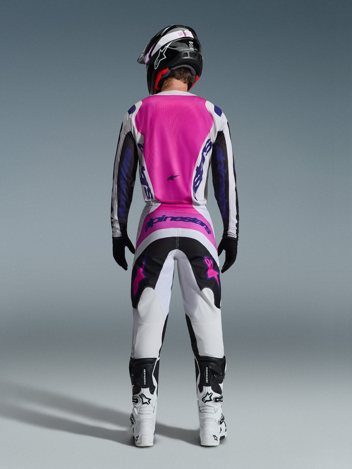 Motocross rider from the back wearing Alpinestars 2026 Fluid Grid Pants and matching jersey, Pink White and Black with Purple branding, Black helmet, White and Black boots, coordinated racing outfit for off-road motocross