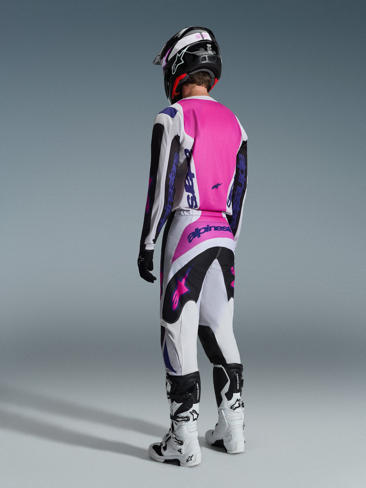 Alpinestars 2026 Fluid Grid Pants, Motocross Pants, Black Light Gray and Purple, rear view of rider wearing matching jersey and white boots, featuring bold purple logos and vibrant pink panels, designed for off-road motocross performance.