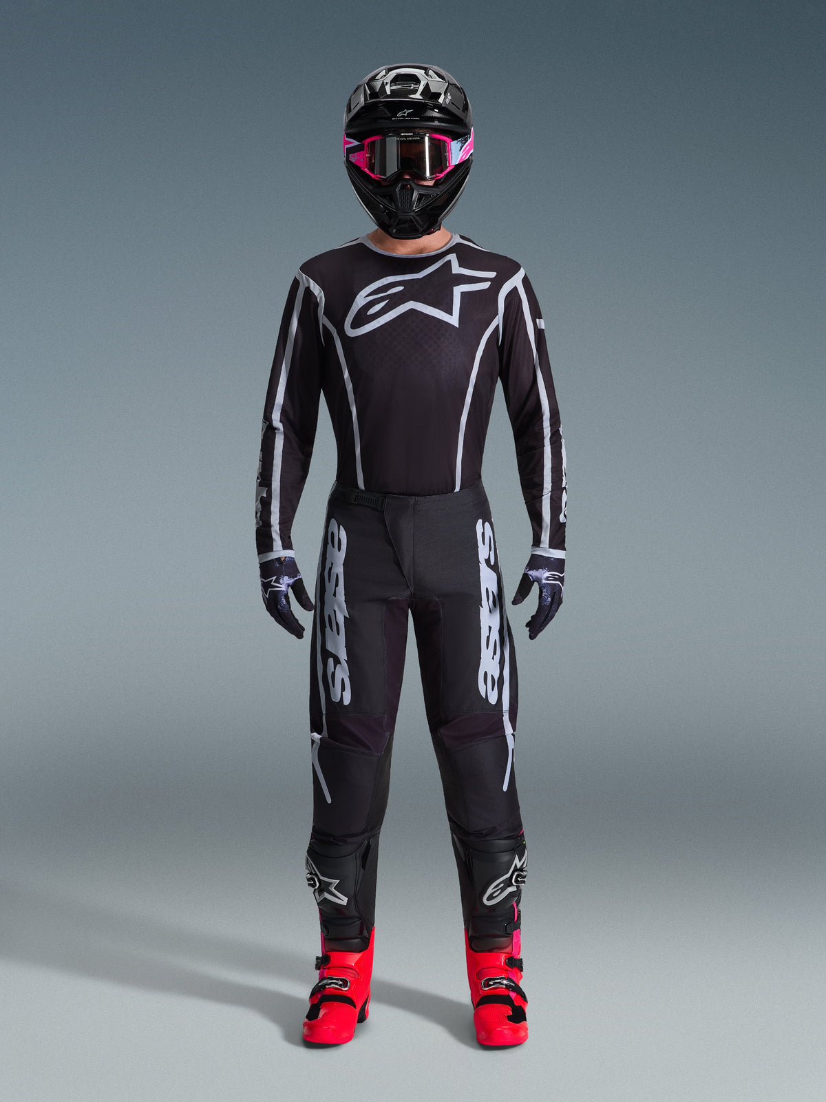 Alpinestars 2026 Fluid Apex Gear Set, motorcross outfit, zwart met grijze accenten, jersey met groot wit Astars-logo, bijpassende broek met opvallende branding, zwarte helm met roze goggles en felrode laarzen, complete off-road racekit