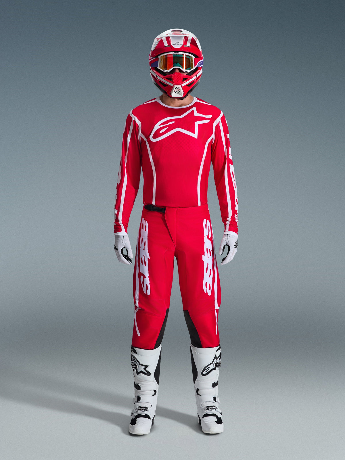 Alpinestars 2026 Fluid Apex Broek, motorcrossbroek, rood en wit, gedragen als een volledige motorcrossuitrusting met een bijpassende rode jersey, witte laarzen en rood-witte helm, voorzien van opvallende branding en zwarte panelen voor off-road prestaties.
