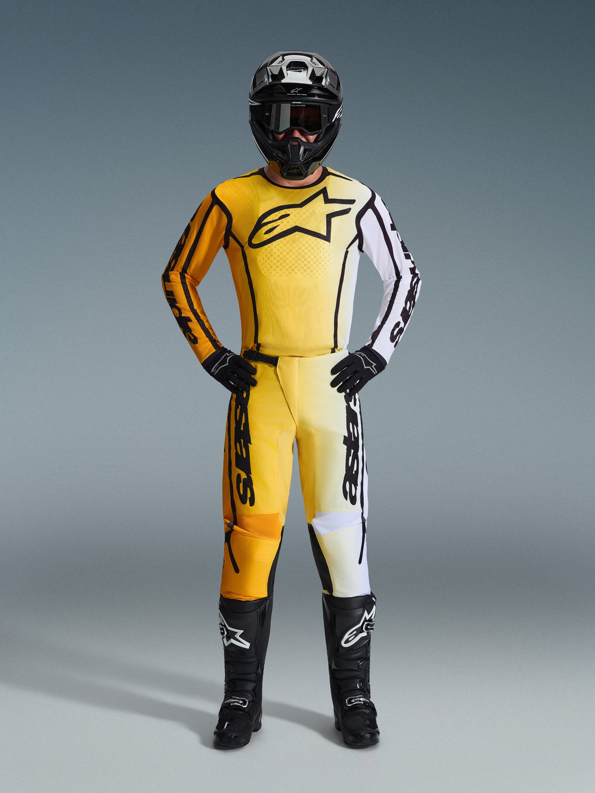Alpinestars 2026 Fluid Apex broek, motorcrossbroek in geel, zwart en wit, gedragen als een compleet racetenue met bijpassende gradient jersey, zwarte helm en laarzen, professionele off-road rijuitrusting.