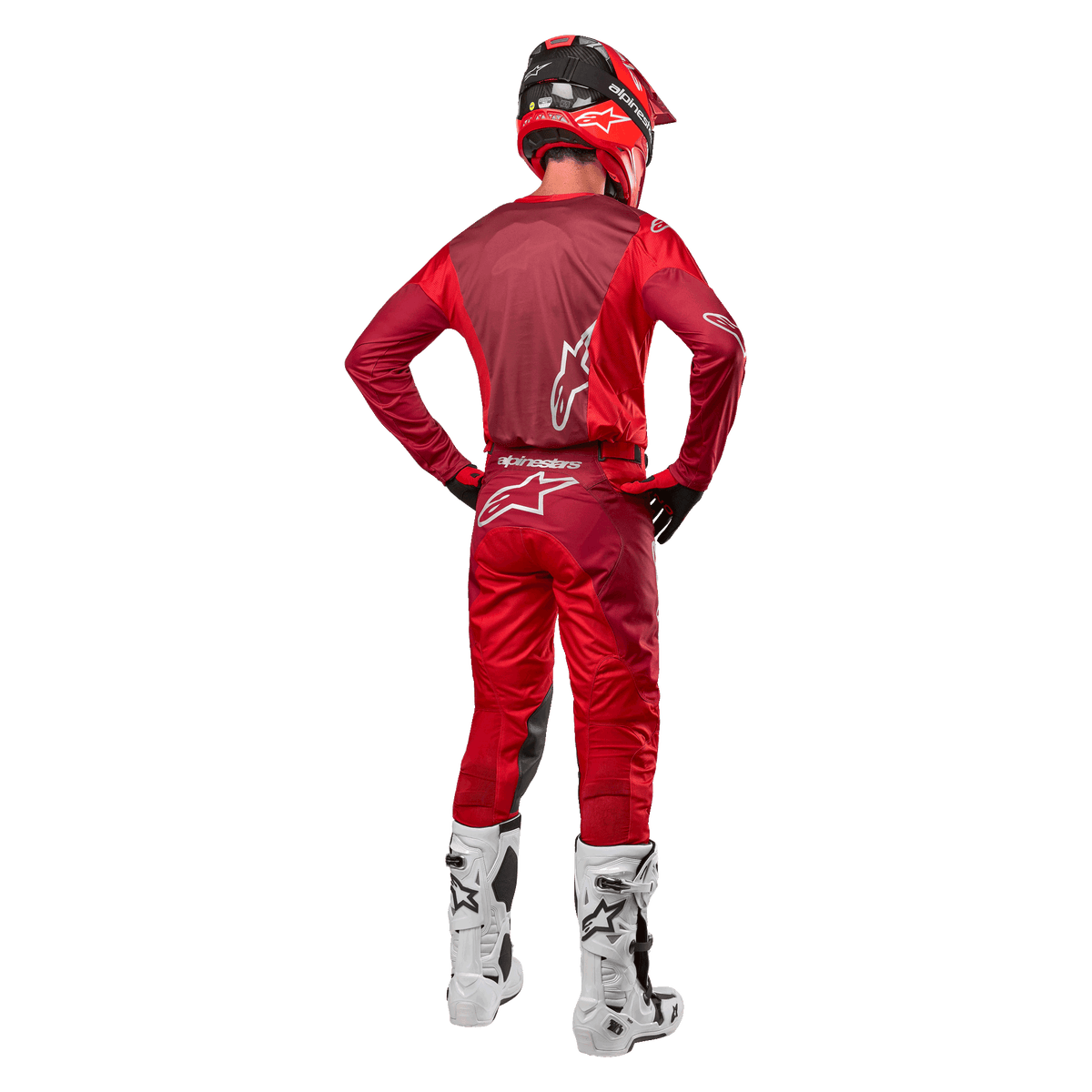 Alpinestars 2024 Racer Hoen broek en bijpassende jersey in Mars Red Burgundy, achteraanzicht van een motorcrossrijder in volledige uitrusting inclusief een rode helm en witte laarzen, toont de sportieve pasvorm en branding voor off-road racen.