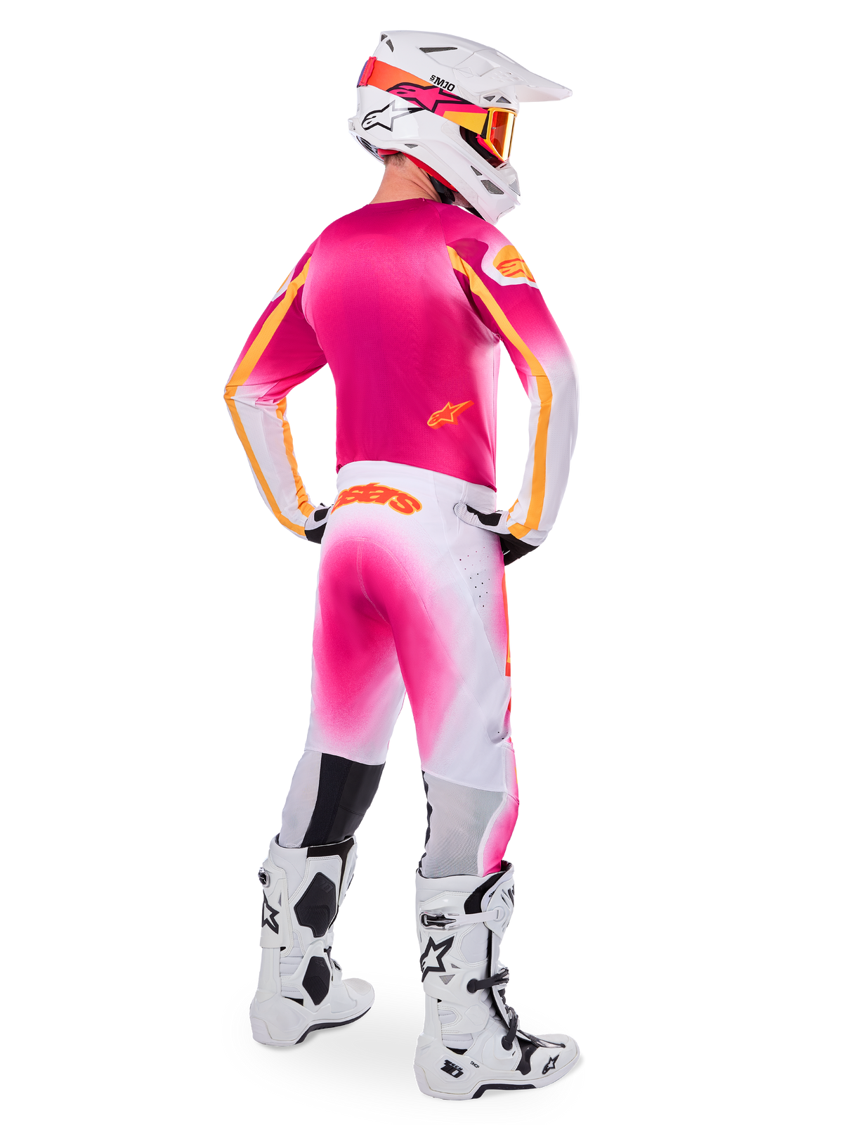 Motocross rider seen from the back wearing the Limited Edition Supertech AFD MIG Gear Set, pink jersey with orange accents, white pants with pink gradient and orange Alpinestars branding, white helmet with pink graphics and orange goggles, white and black boots, professional off-road racing kit
