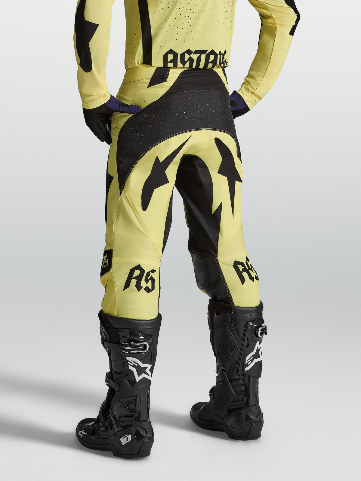 Alpinestars Techstar Atrox broek, atletische motocrossbroek voor heren, geel en zwart, achteraanzicht van professionele off-road race-uitrusting met zwarte Tech 10 motorlaarzen.