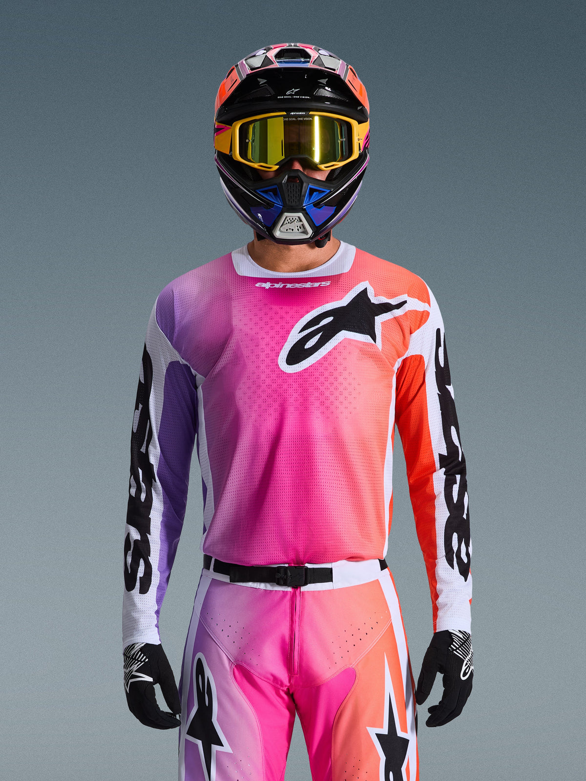 Alpinestars 2026 Racer Air Portl Jersey, motorcross jersey, levendig roze, paars en oranje kleurverloop, gedragen met een bijpassende helm en bril, voorzien van een groot zwart ster-logo op de borst, ademende mesh-constructie, performance-kleding voor off-road racen
