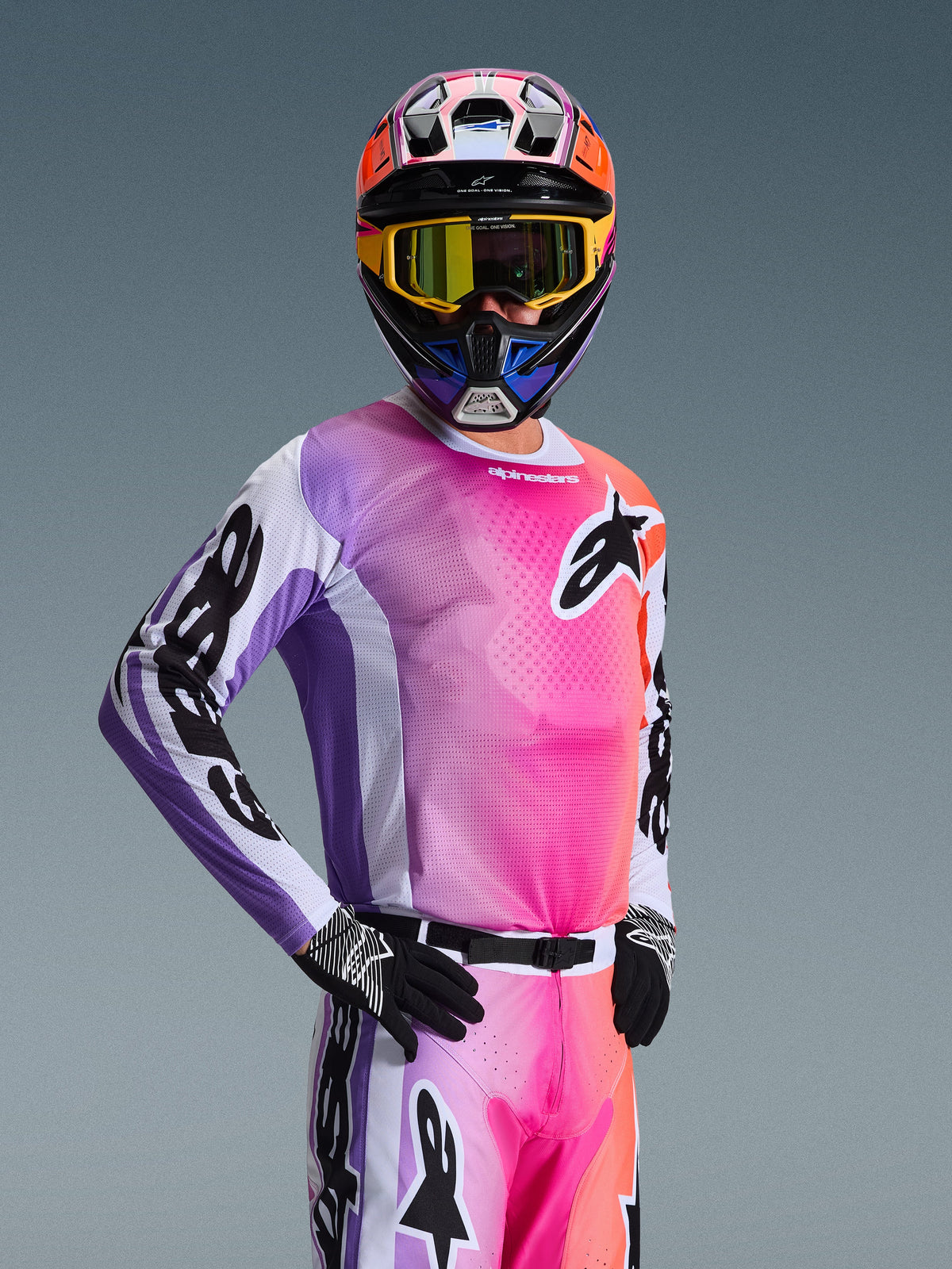 Motorcrosser in de Alpinestars 2026 Racer Air Portl Jersey, meerkleurig roze, paars en oranje kleurverloop met witte accenten, bijpassende kleurrijke helm en gele crossbril, zwarte handschoenen, professionele off-road race-uitrusting