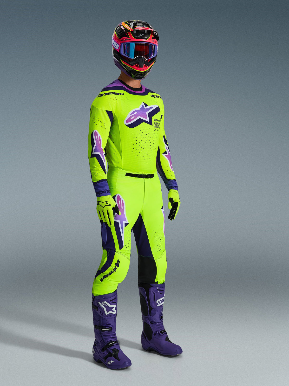 Motocrossrijder die de 2026 Supertech Vista Jersey draagt, felgeel met paarse en zwarte accenten, bijpassende gele motocrossbroek, paarse laarzen en gele handschoenen, veelkleurige helm met blauwe crossbril, hoogwaardige race-uitrusting voor off-road competitie