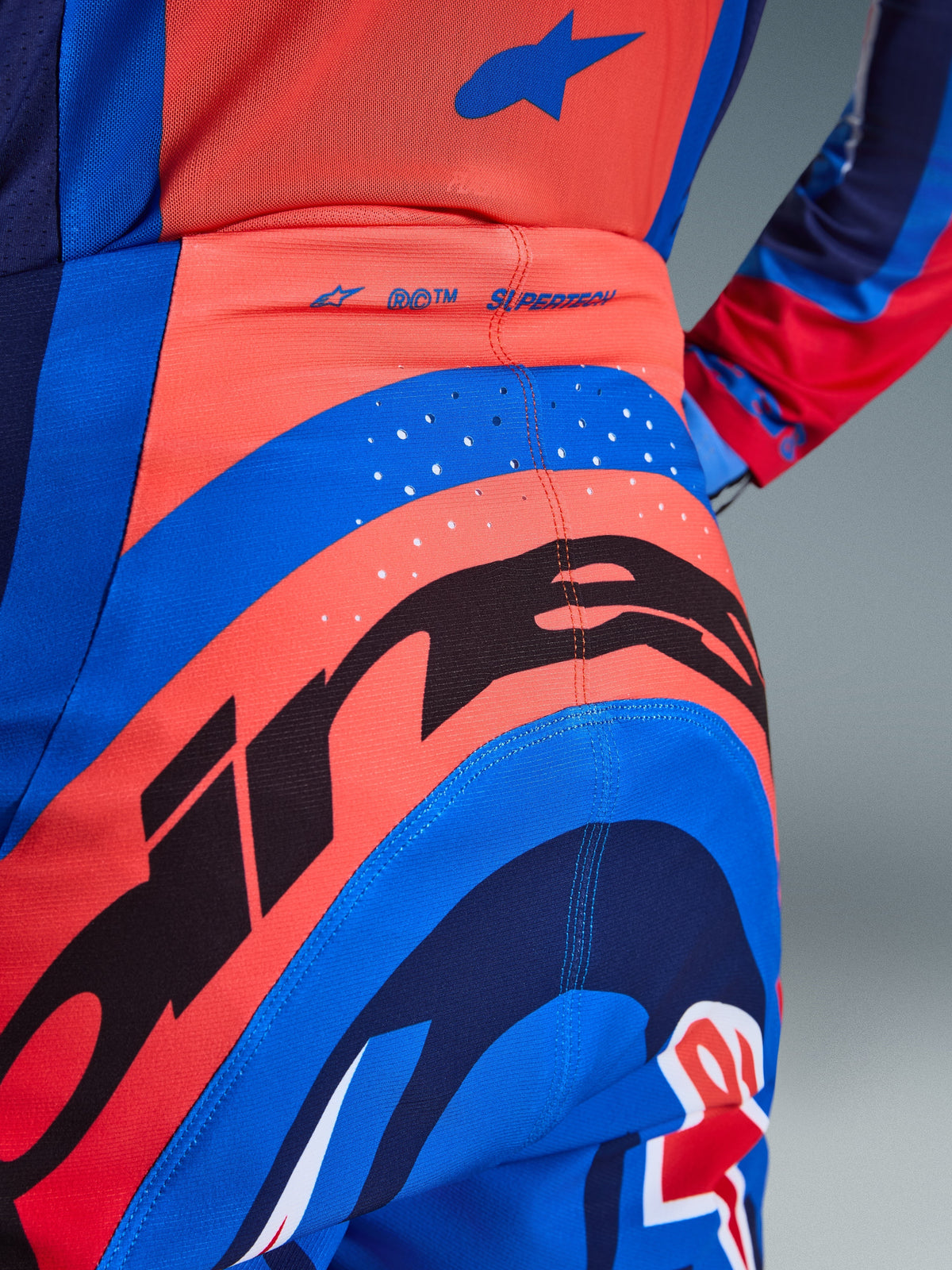 Alpinestars 2026 Supertech Vista Pants, Motocross Pants, Dark Navy Hot Coral and Cobalt, close-up rear view showing bold branding, laser-cut perforations for ventilation, and 'SUPERTECH' logo on the waistband, performance stretch material for off-road racing